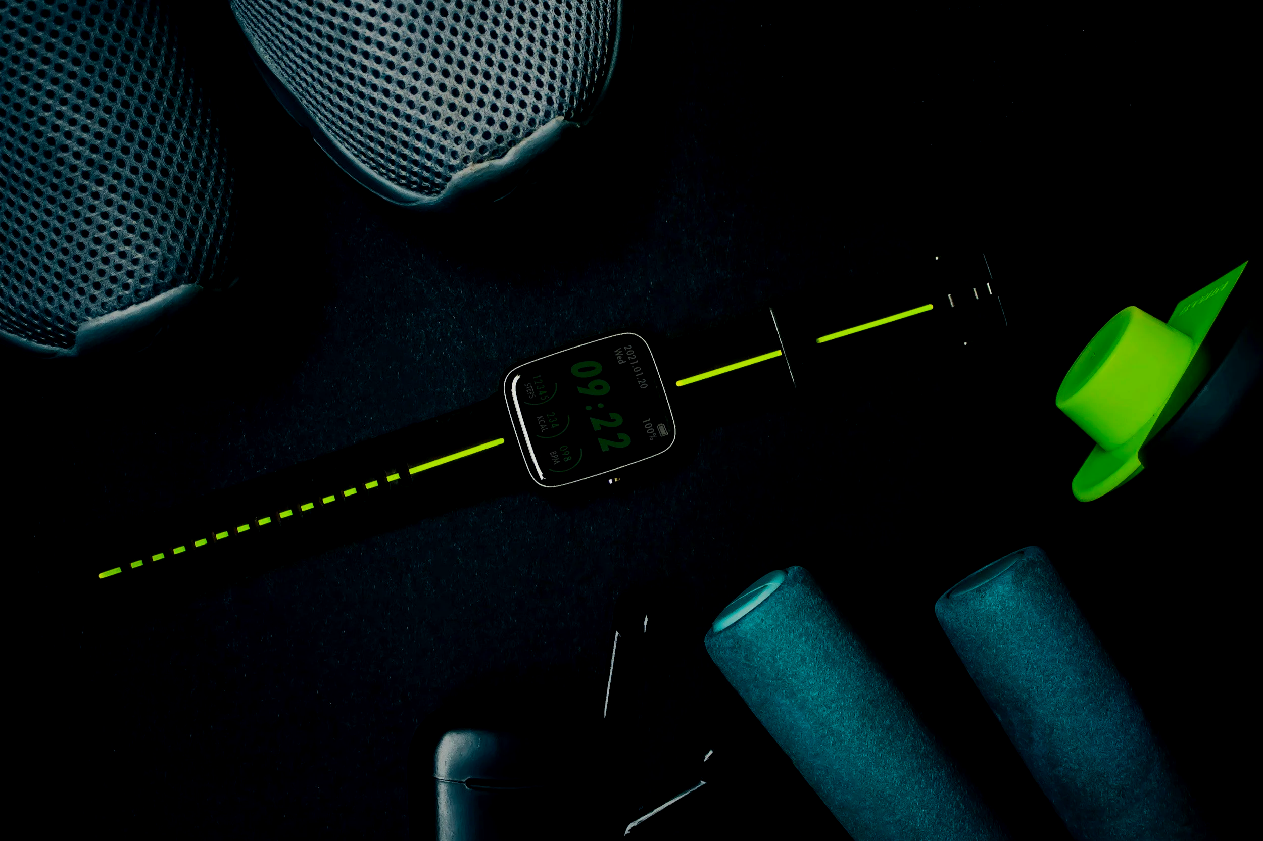 fitness gear and devices placed on a black surface next to foam rollers.