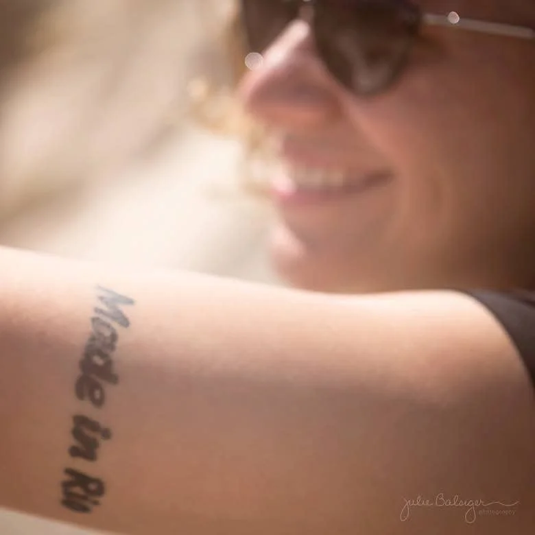 Karina, creator of Going to Rio, smiling and showing a tattoo on their arm that reads 'Made in Rio'