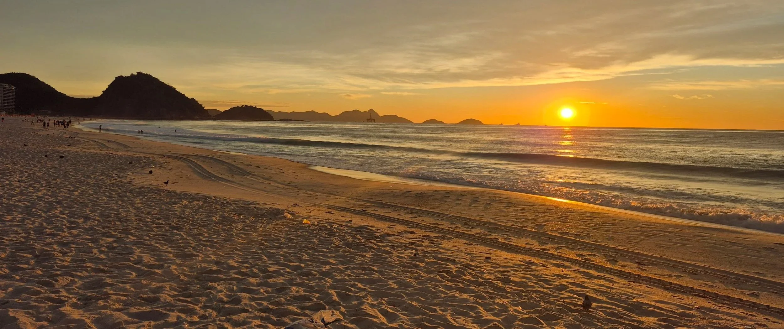 Sunrise over Copacabana Beach, Rio de Janeiro, with golden light reflecting the mountains in the background.