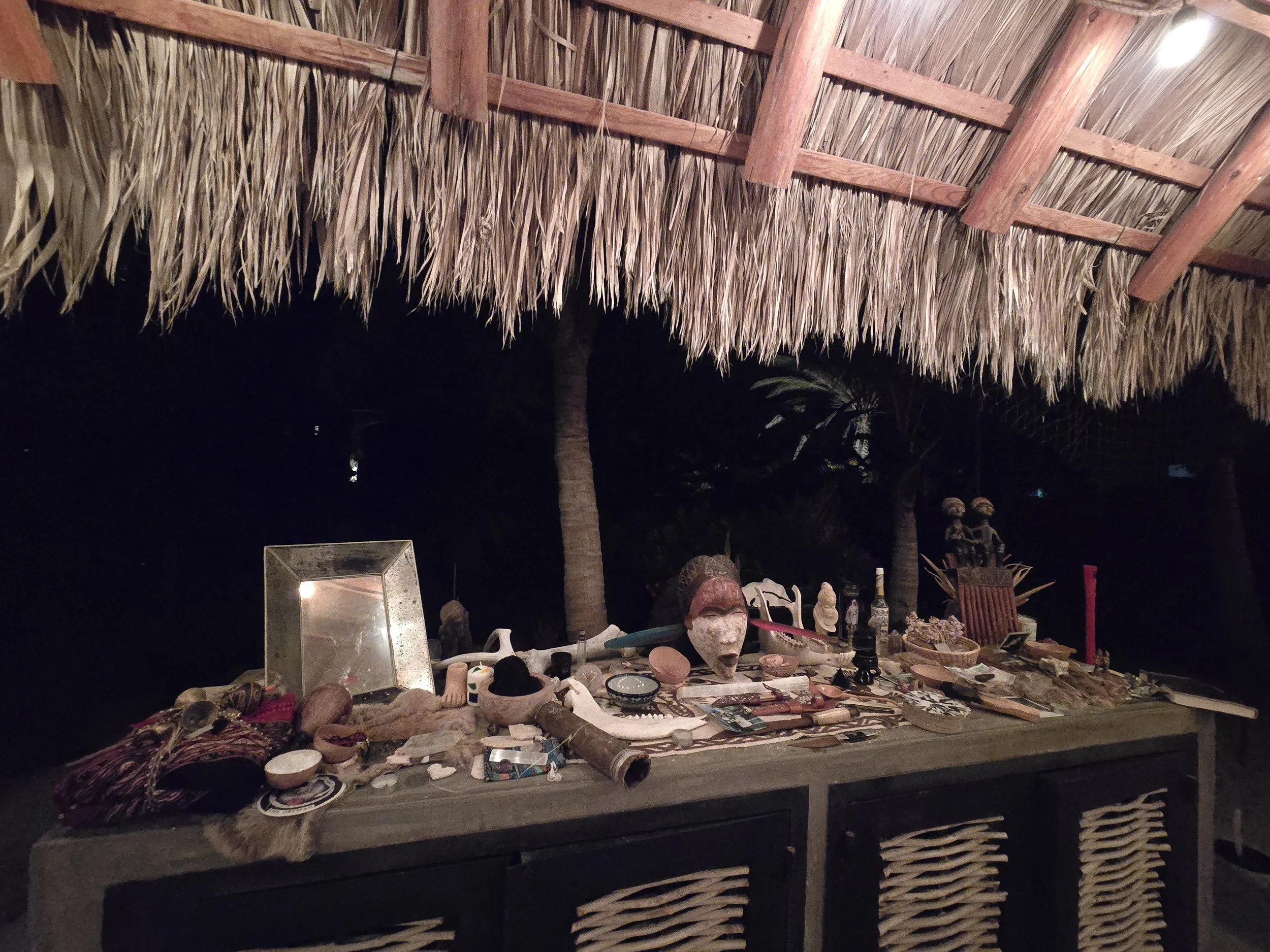 Table with Indigenous art and artifacts, under a thatched roof at night.
