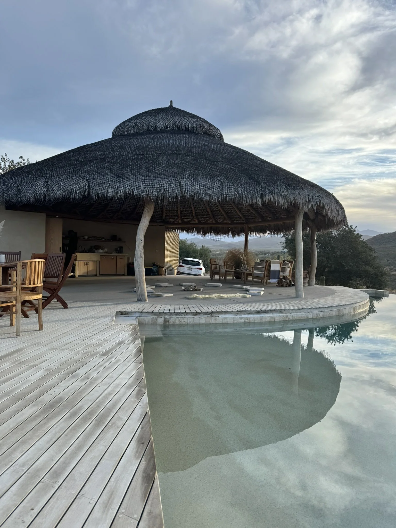 A resort with a thatched-roof cabana over a pool, surrounded by outdoor furniture and scenic mountains in the background.