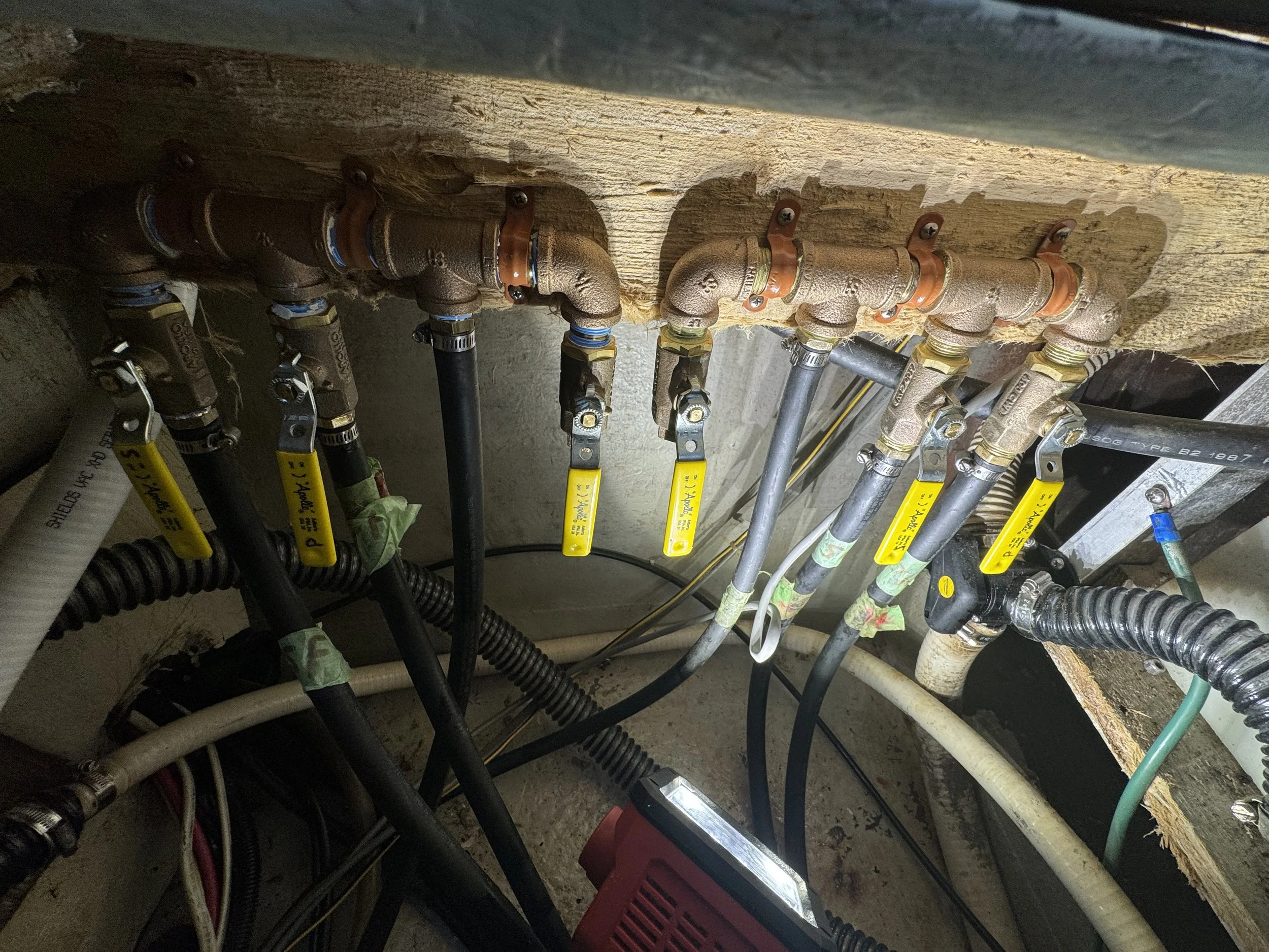 A plumbing system with multiple brass and black pipes, valves with yellow handles, and connecting fittings in an indoor setting.