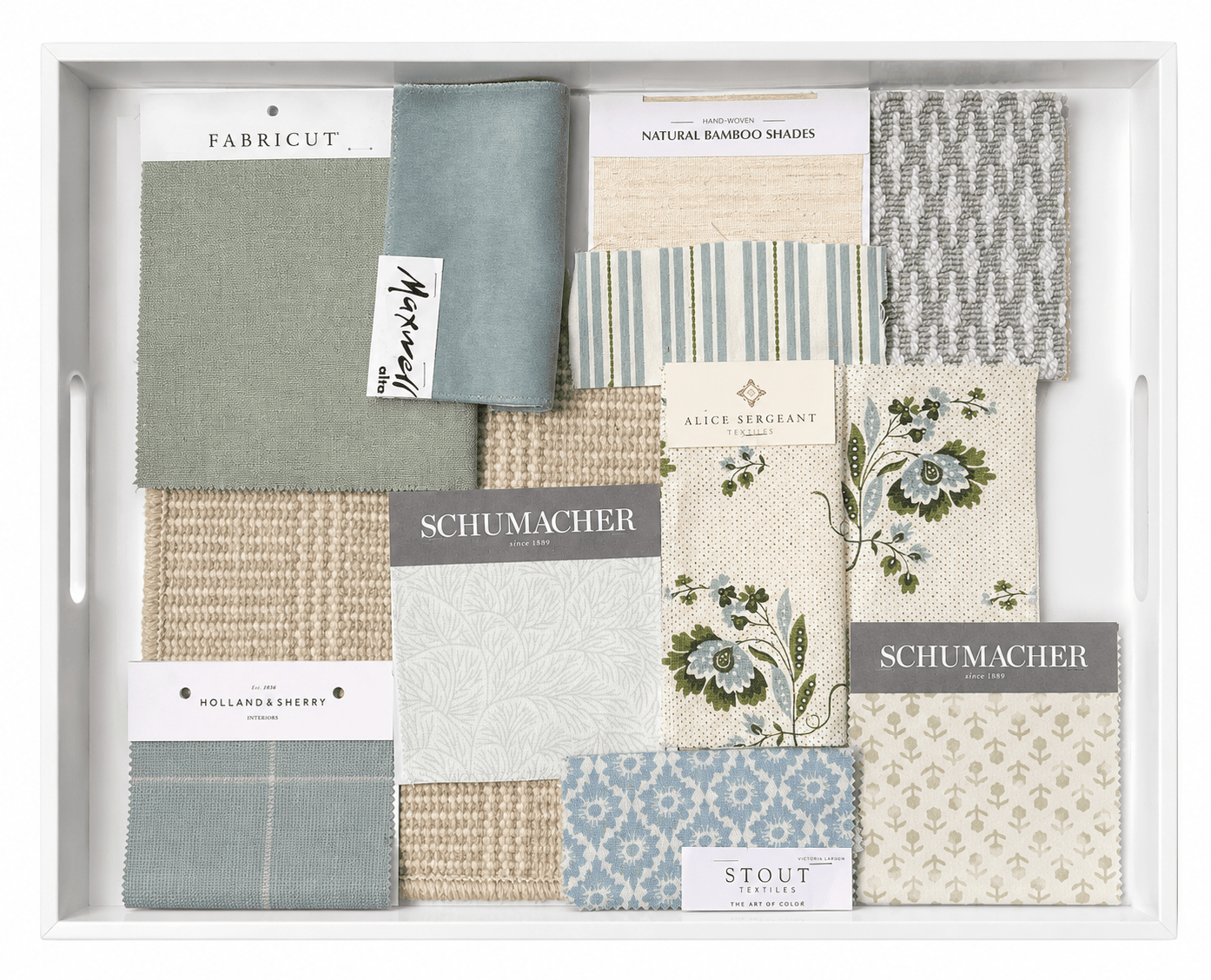 A white tray containing fabric swatches in various shades of blue, green, beige, and gray, with labels from brands like Schumacher, Alice Sergeant, and Holland & Sherry.