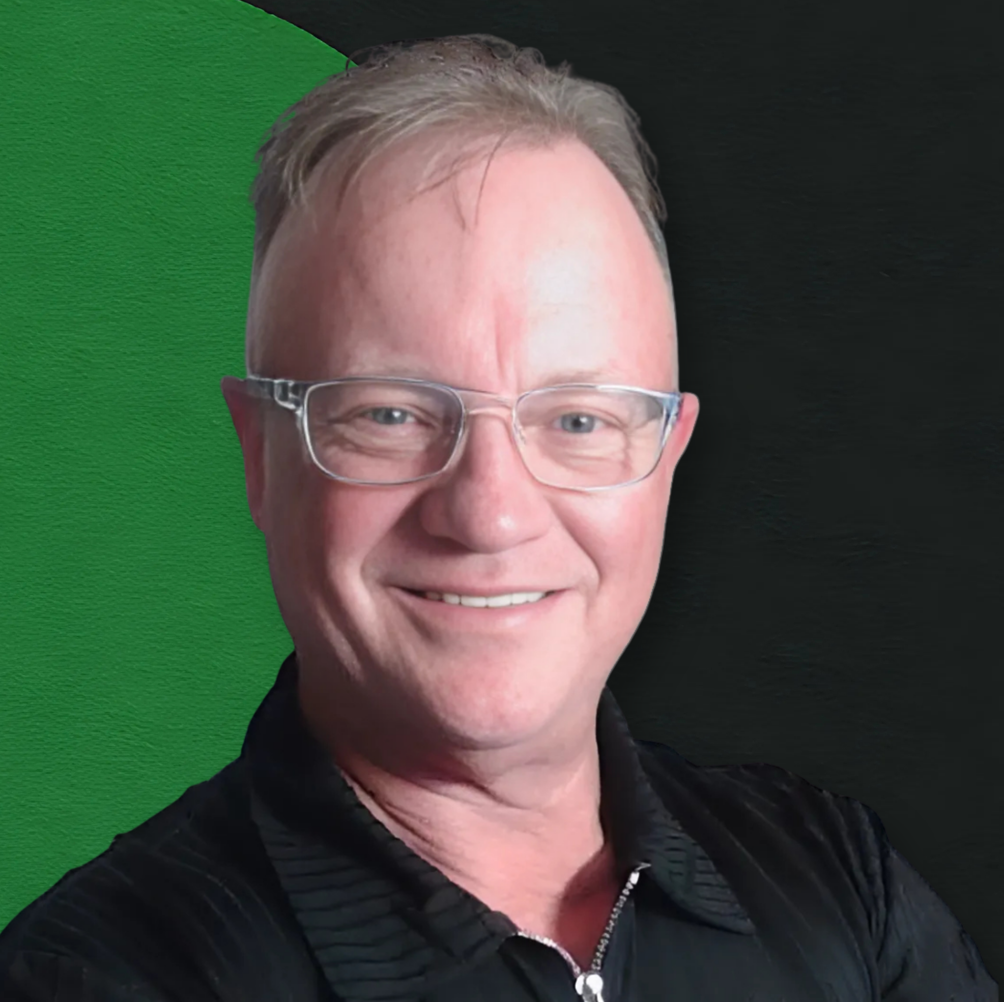 Close-up of a man with gray hair, glasses, smiling, with a dark background and a green screen behind him.