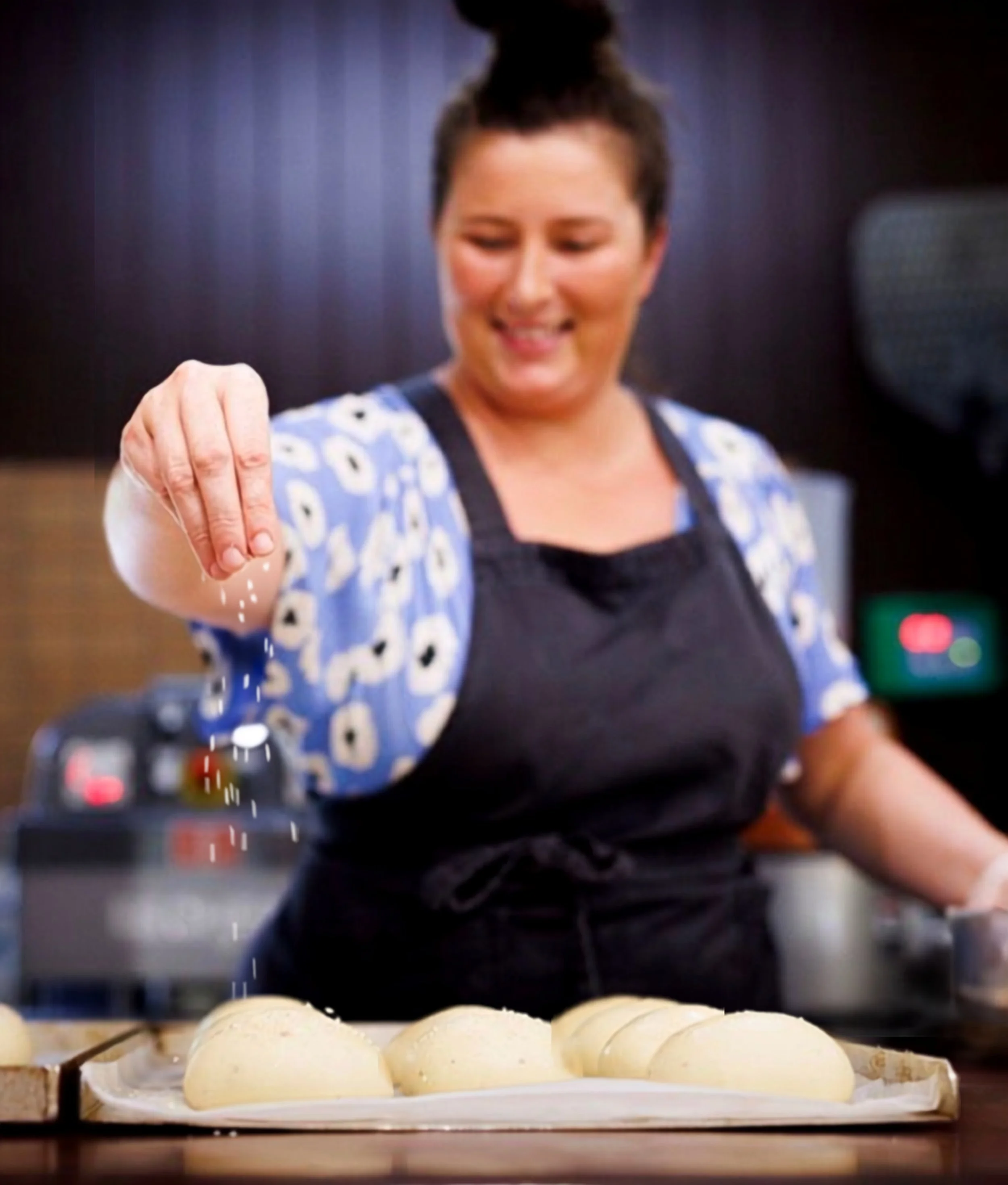 Person slicing a loaf of rustic bread on a wooden cutting board, with a cloth underneath, against a plain background.