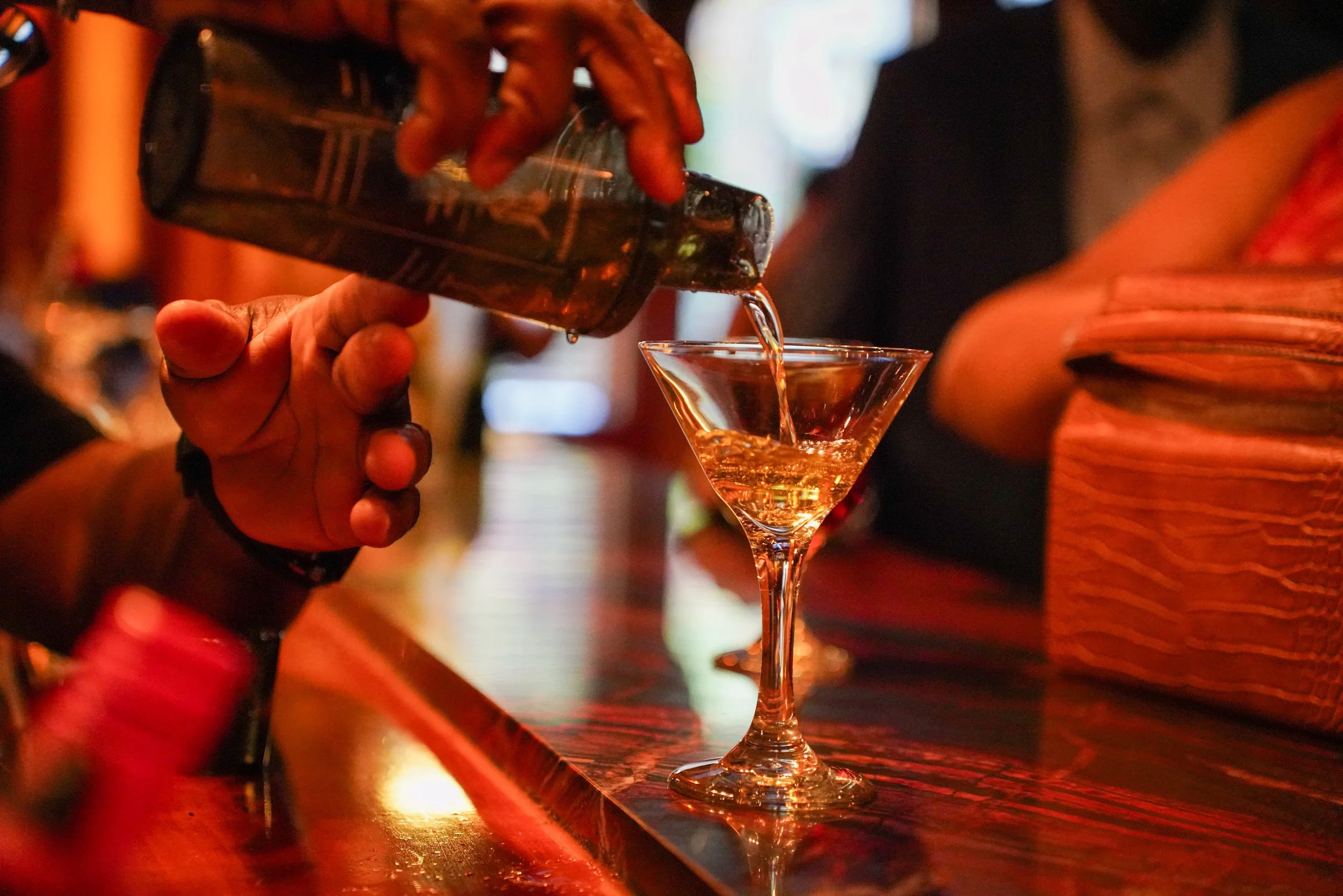 Person pouring a drink into a martini glass at a bar.