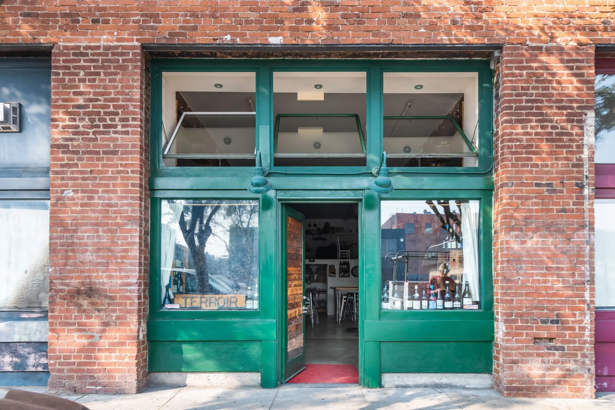Green storefront entrance with glass windows and door, brick building exterior, and outdoor view of trees and buildings.