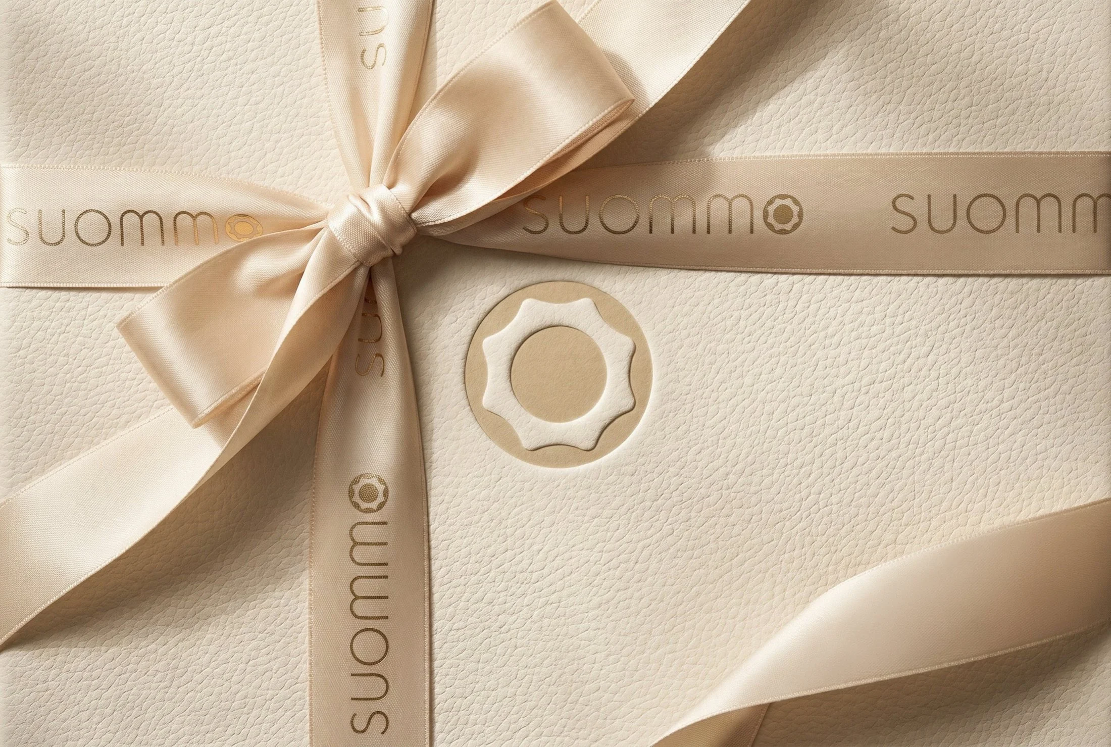 Inside SUOMMO, a textured SUOMMO presentation box with branded satin ribbons, a bow and the emblem.