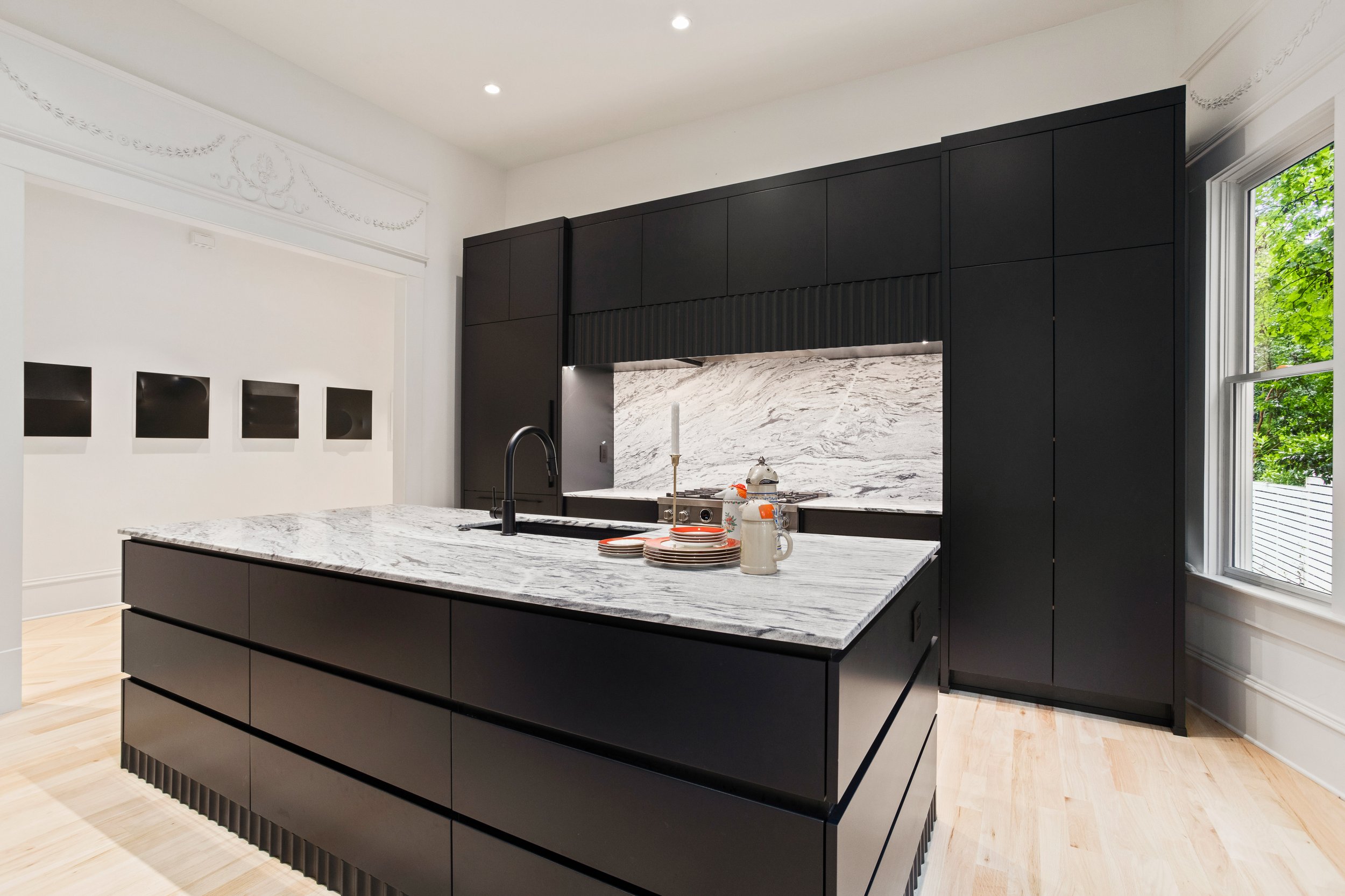 This dramatic kitchen balances restraint and impact. Custom cabinetry is designed to read as freestanding furniture, seamlessly concealing all appliances for a clean, cohesive look. Anchoring the space, a substantial island delivers generous work sur