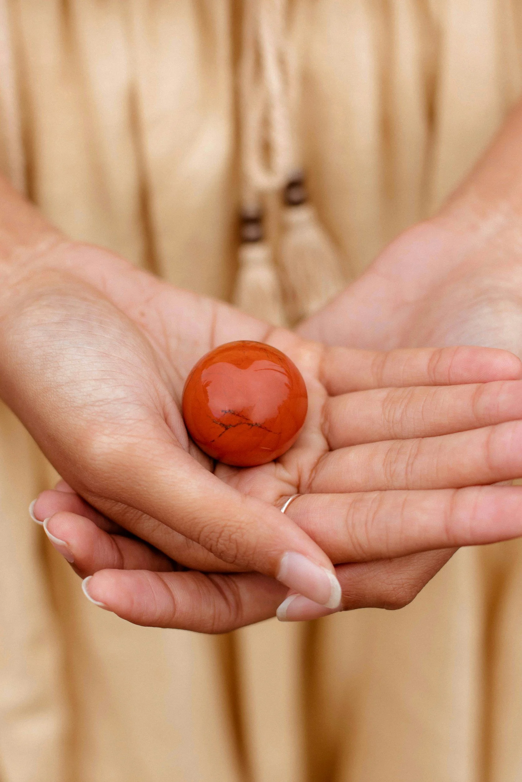 Red-orange carnelian stone in a sphere shape in the palm of a human.
