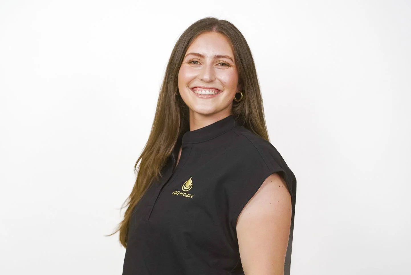A smiling woman with long brown hair wearing a black sleeveless polo shirt with the logo 'LUV MOBILE' on the chest, standing against a white background.