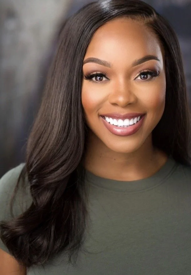 Close-up photo of a smiling young African American woman with straight long dark hair and makeup, wearing a green top.