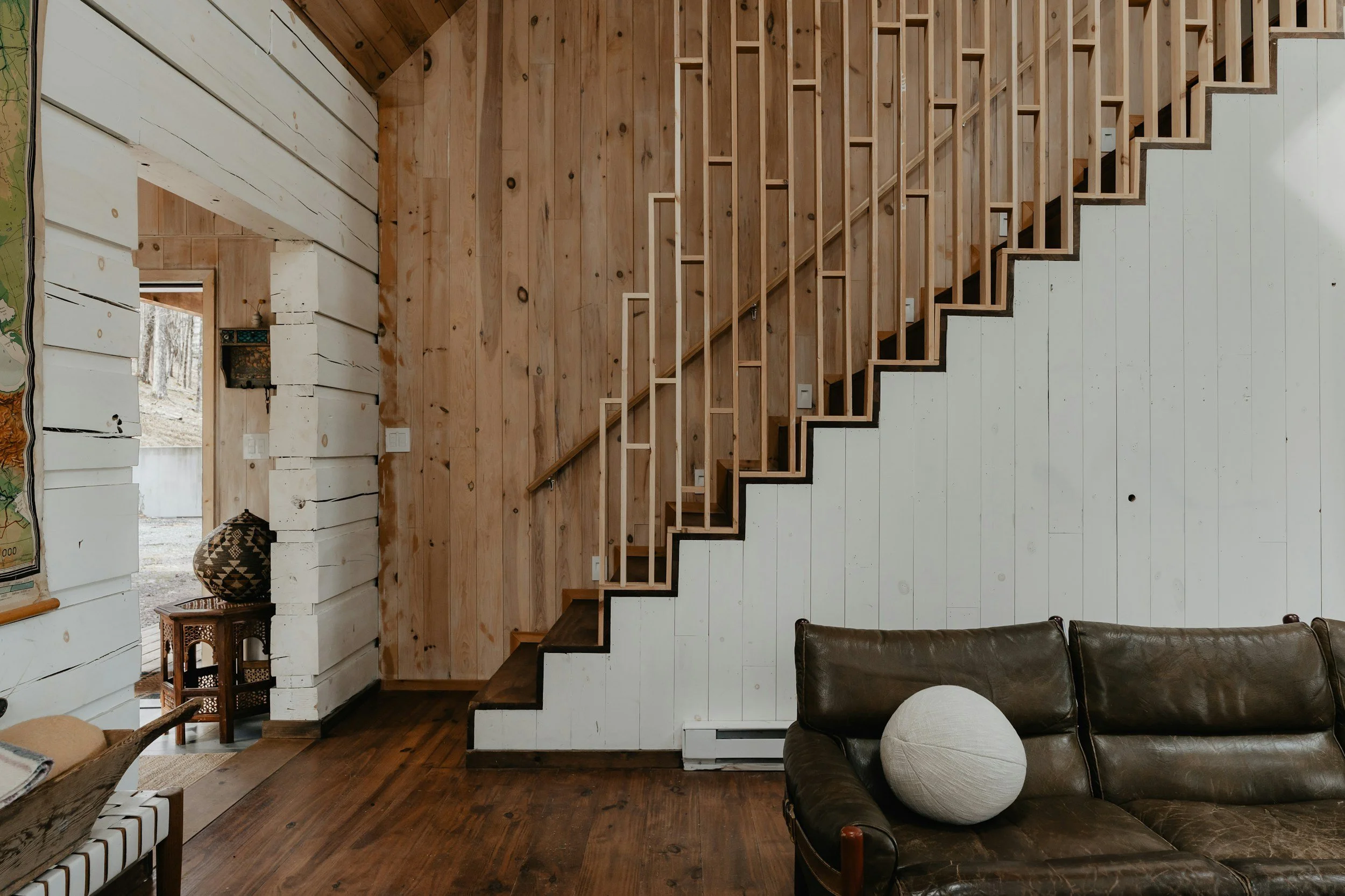 Interior view of a room with wood-paneled walls, a staircase with wooden railing, and a leather sofa with a round pillow.