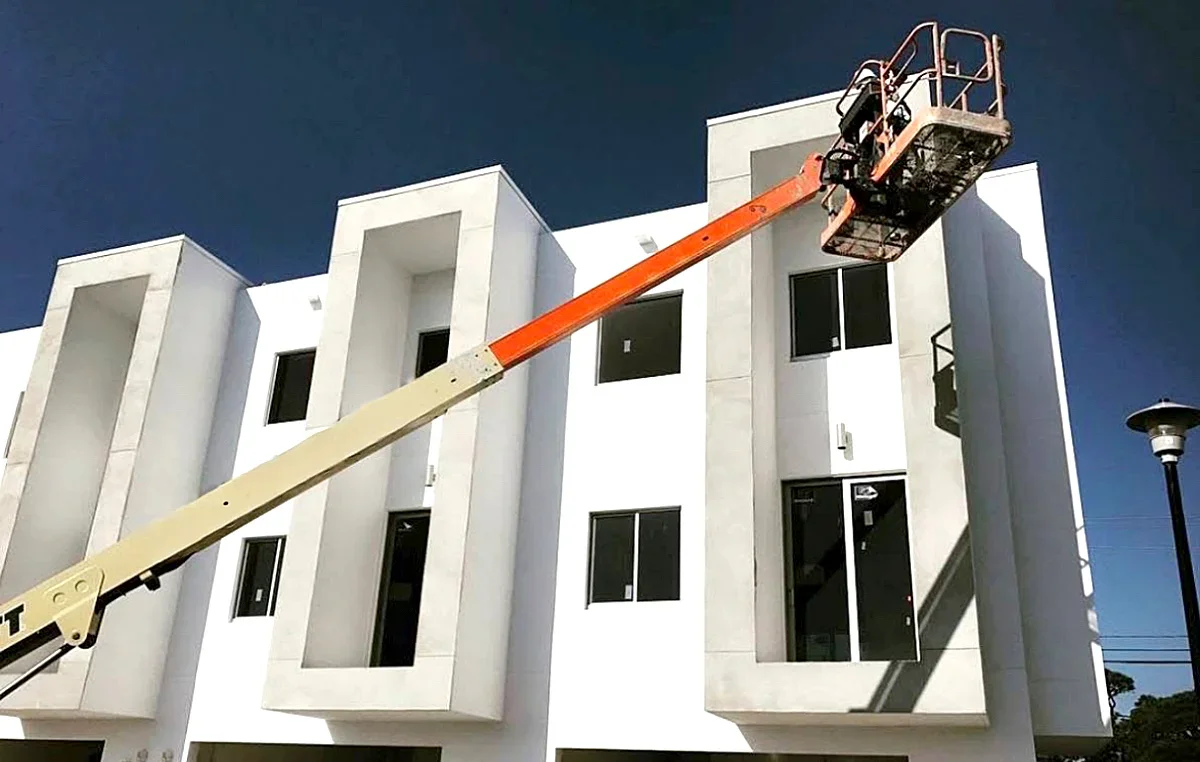 A construction lift extends towards the upper level of a modern white building under clear blue sky.