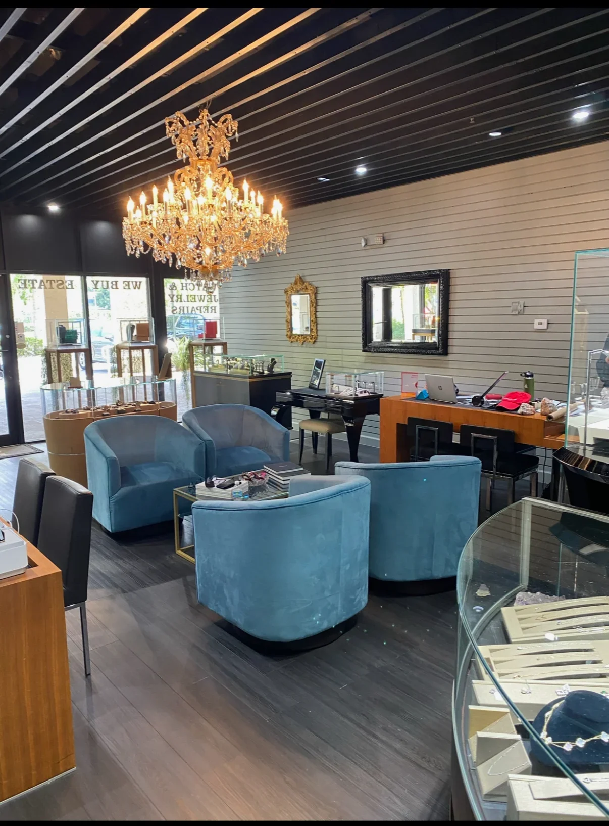 Interior of a jewelry store with blue velvet chairs, a glass display case, a chandelier, and various mirrors on the walls.