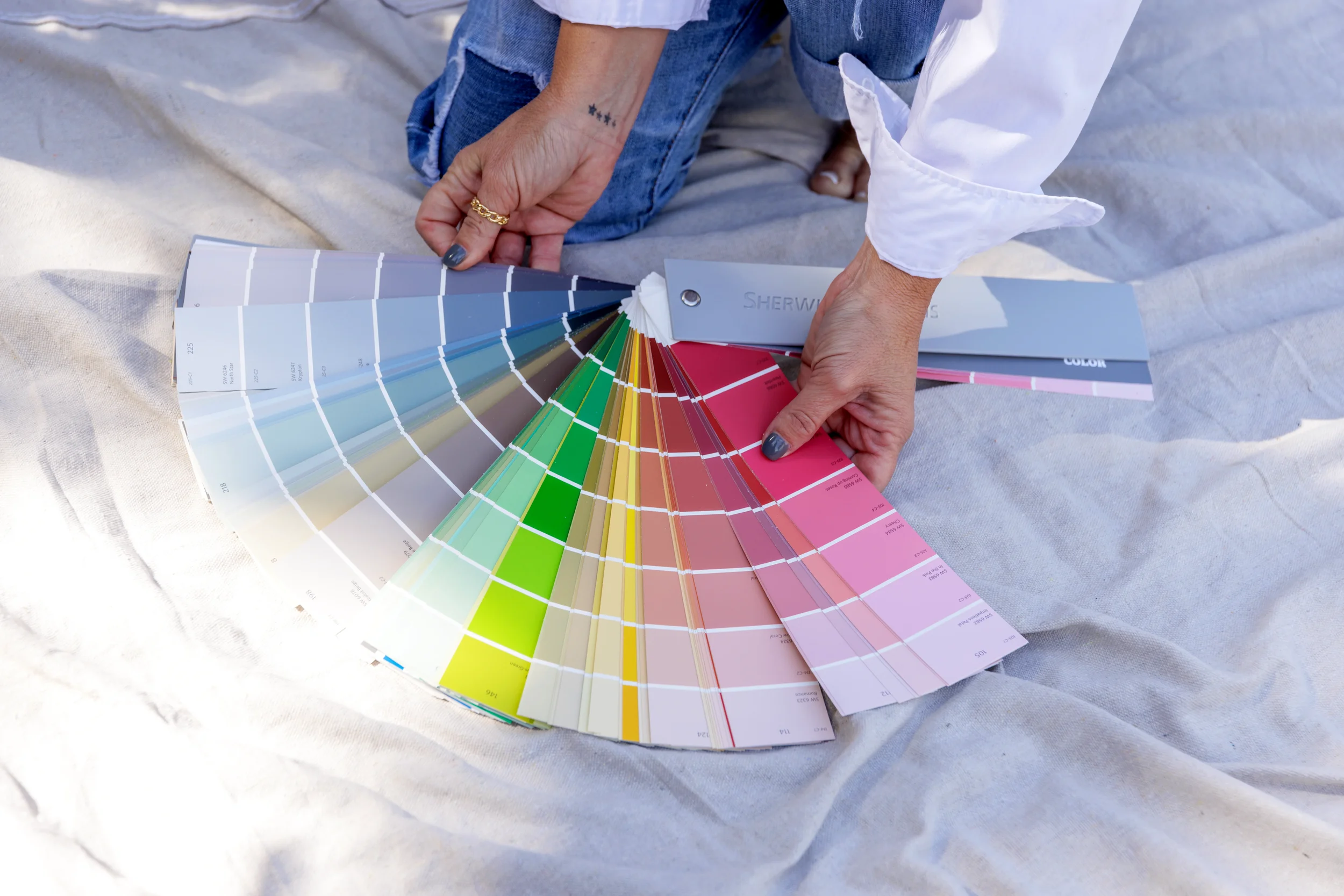 Person holding a fan deck of color swatches outdoors, with fabric underneath.