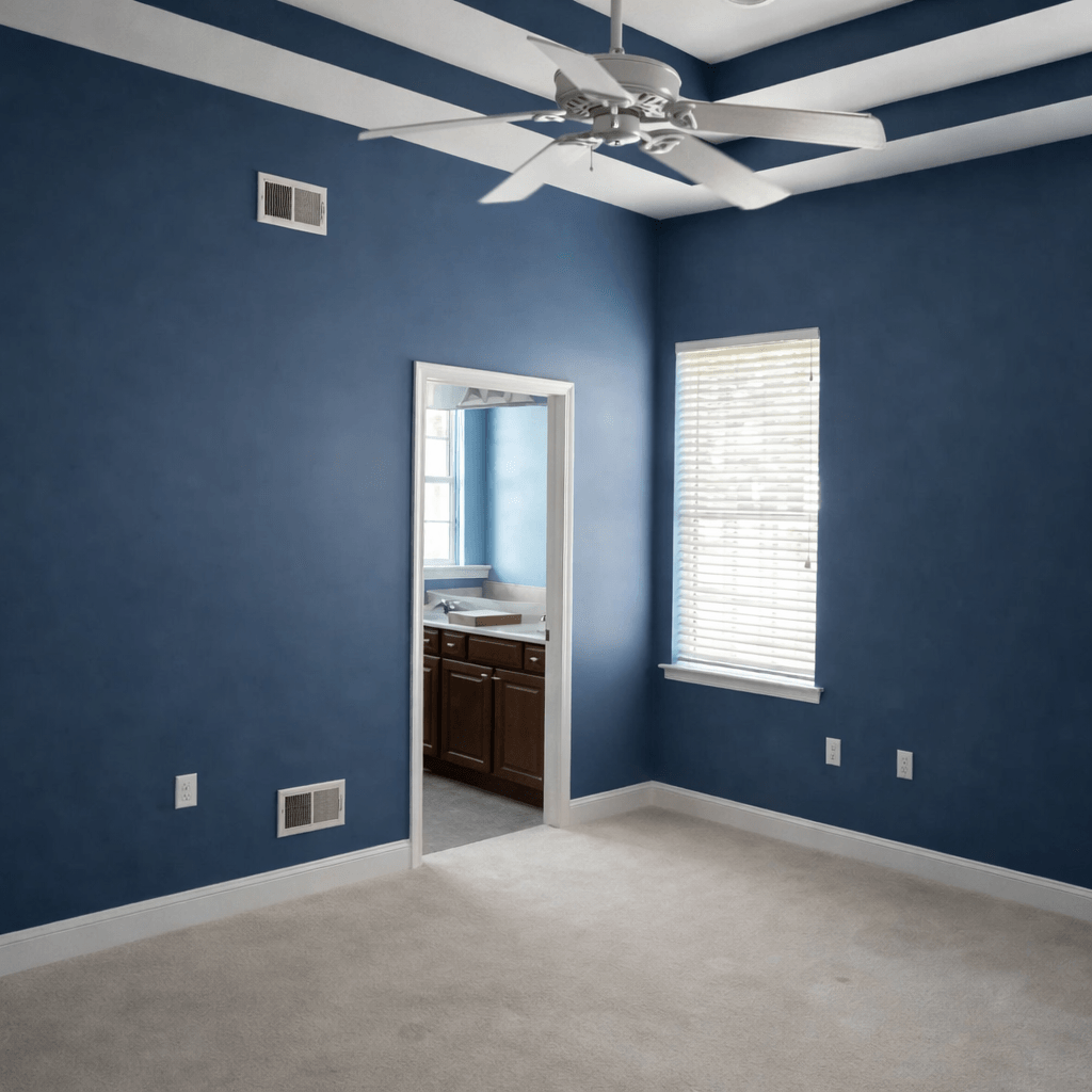 Empty bedroom with blue walls, white carpet, ceiling fan, window with blinds, and an open door leading to bathroom with wooden vanity and sink.
