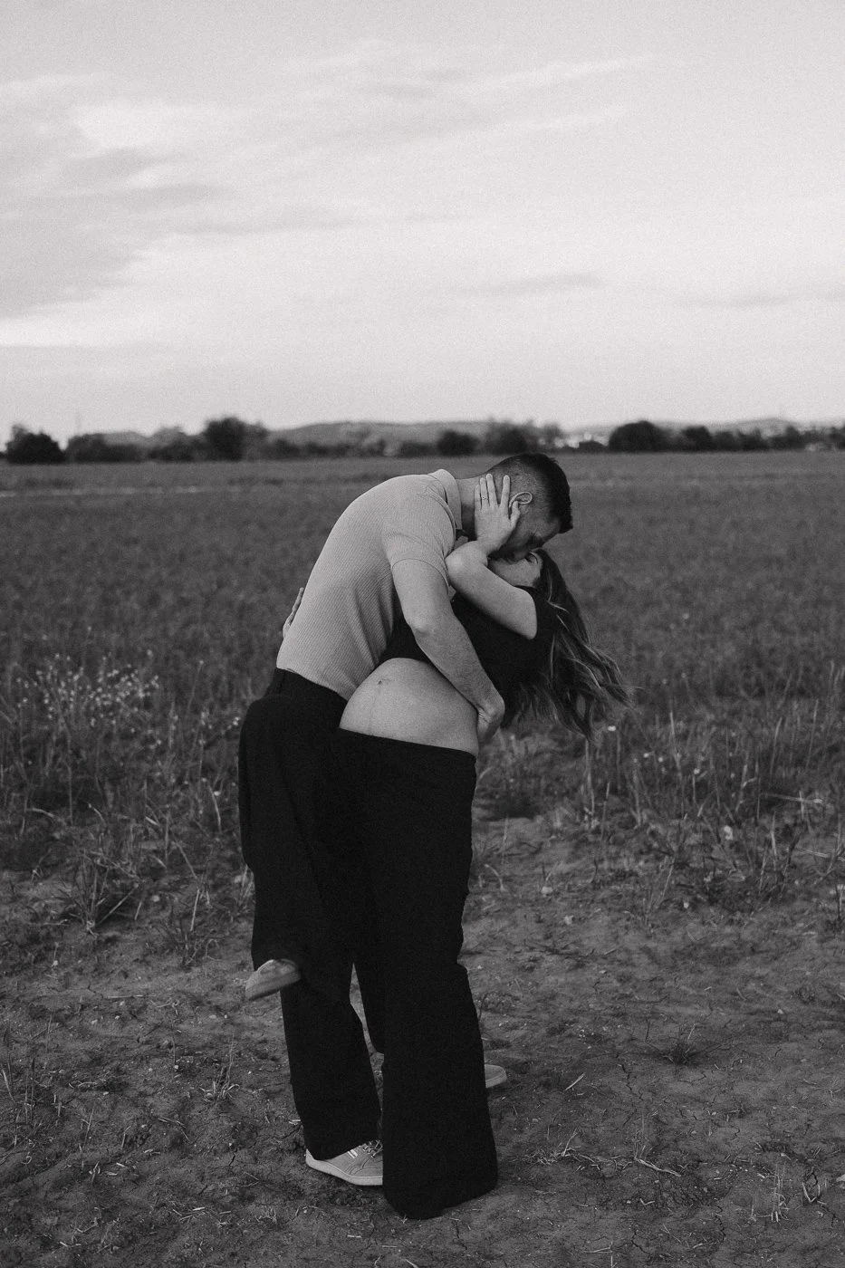 Pareja besándose en un campo abierto, en un entorno natural con cielo y horizonte amplio.