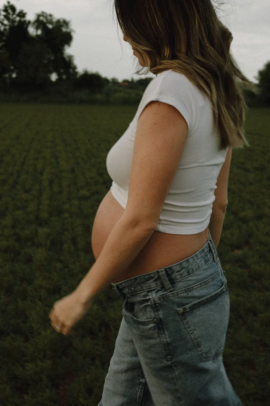 Mujer embarazada con camiseta blanca y jeans en campo de cultivo.