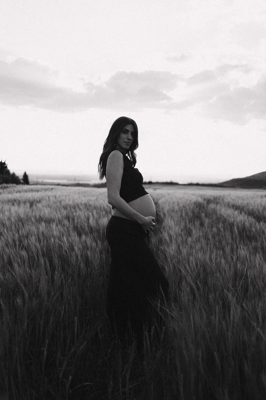 Mujer embarazada en un campo de trigo en un entorno natural, en blanco y negro.