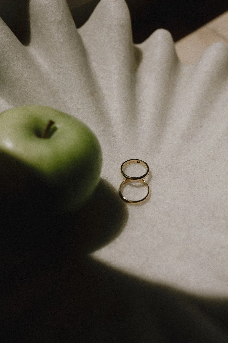 Una manzana verde, un anillo dorado y una superficie de tela clara con pliegues.