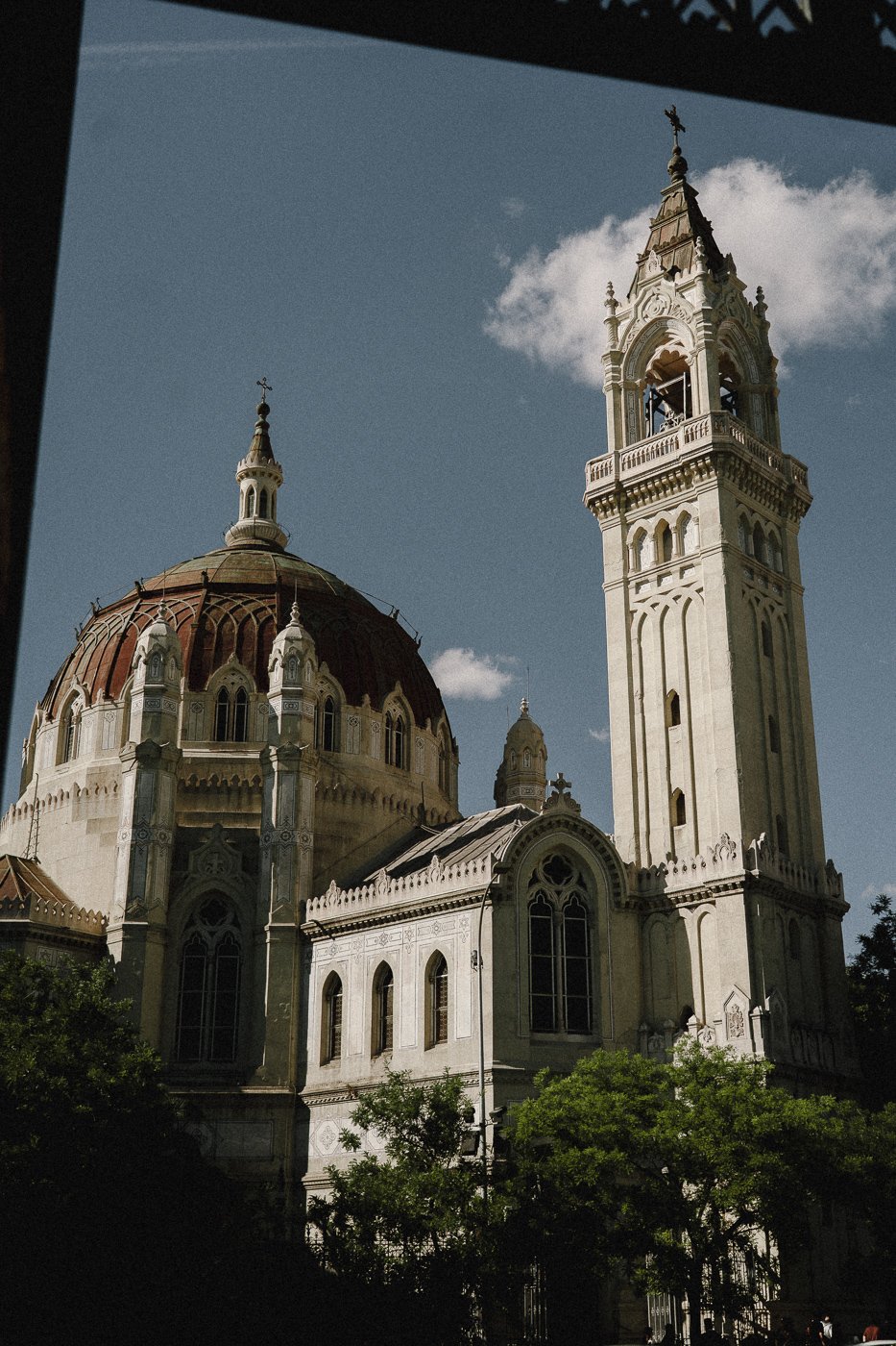 Vista de una iglesia con cúpula grande y torre con campanario, en un día soleado con cielo azul y algunas nubes.