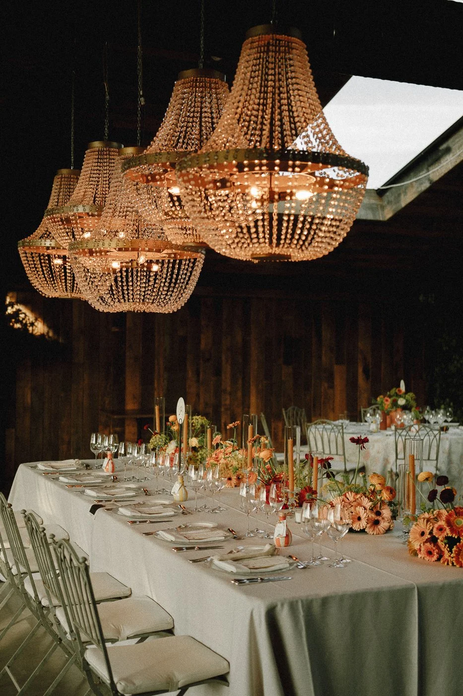 Mesa decorada para evento con flores y velas, colgantes de candelabros y sillas alrededor.