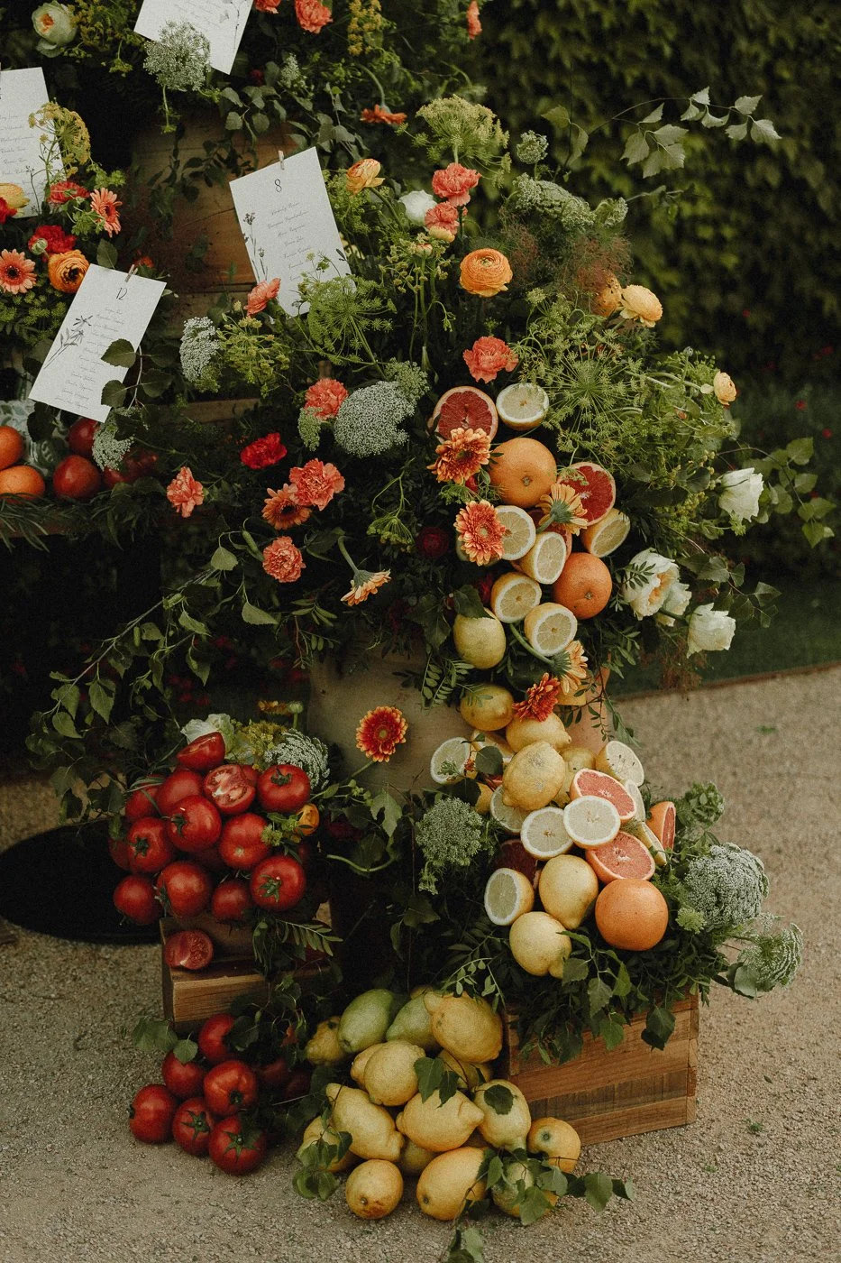 Arreglo de frutas y flores con notas y etiquetas decorativas en un entorno natural.