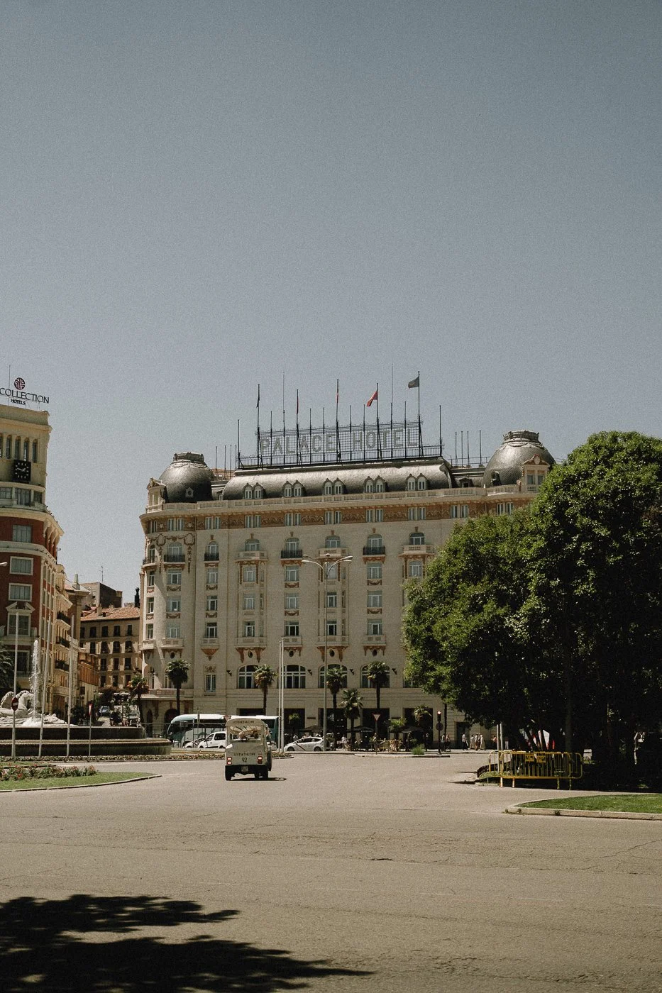 Vista de un edificio con cartel que dice 'PALACE HOTEL' en lo alto en un día soleado, con árboles y coches en la calle frente al hotel.