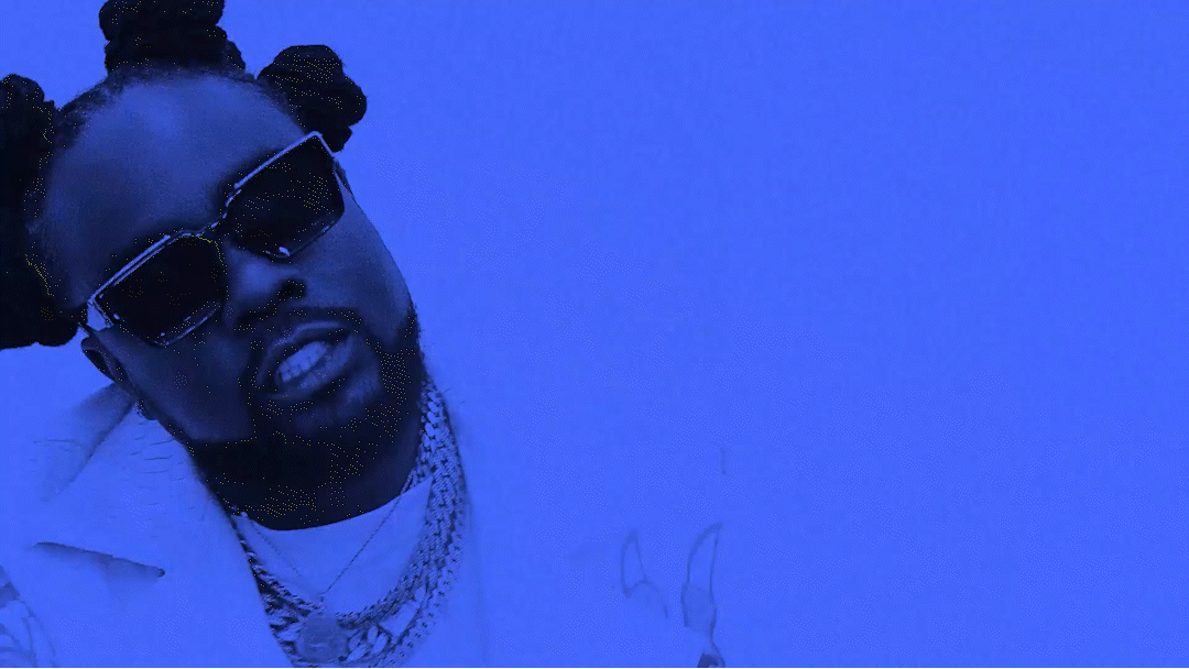 A man with braided hair wearing sunglasses and multiple necklaces, posing in front of a blue background.