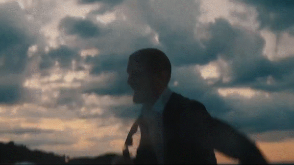 Silhouette of a man in a suit and tie against a cloudy sky during sunset.