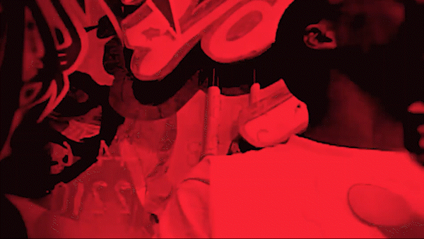 Person in dark clothing with red lighting, possibly holding a phone or device, in a dim environment.