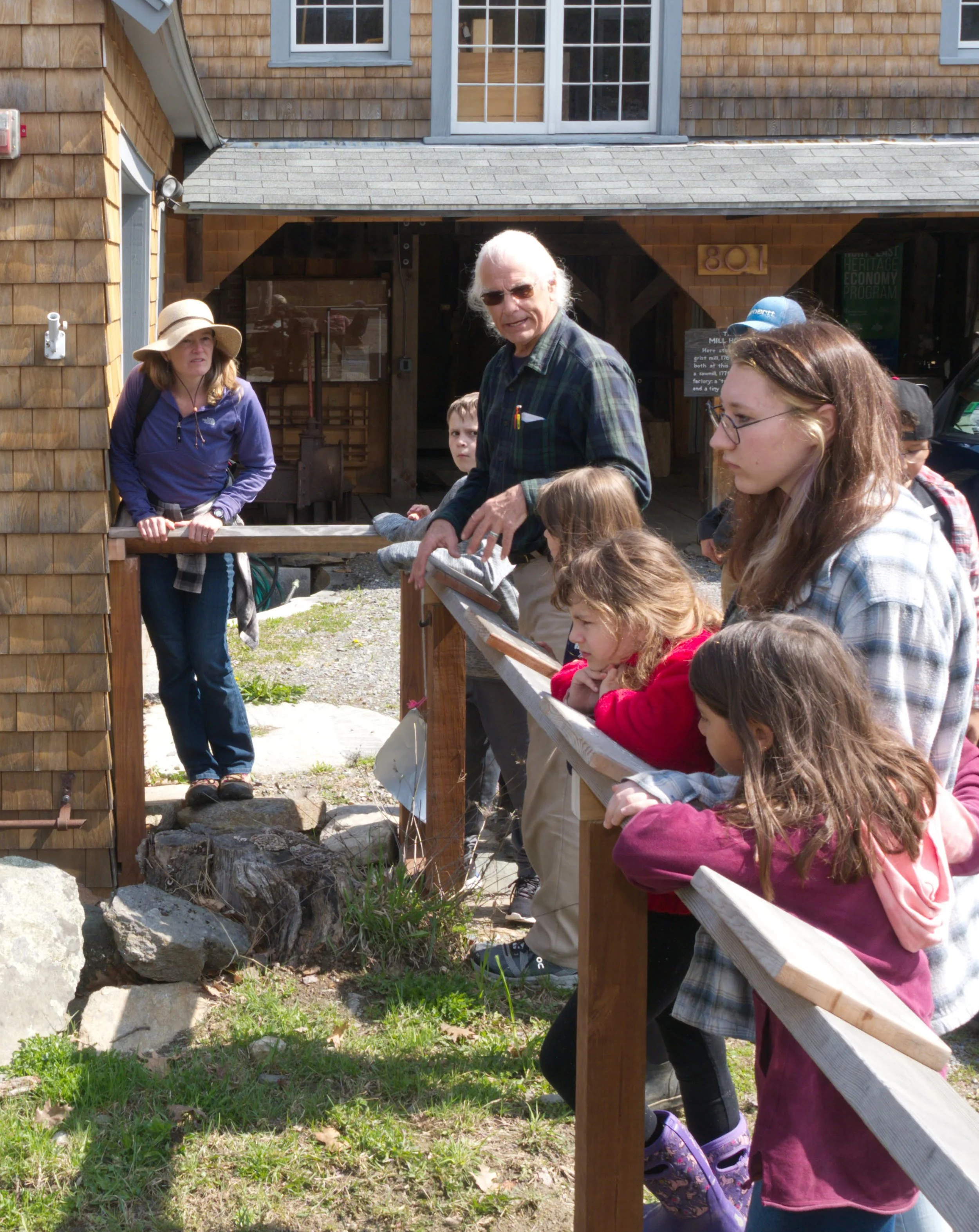 Children and adults outdoors at Chase's Mill looking at something outside the photo frame