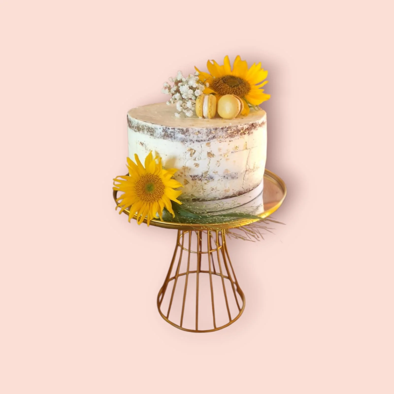 Ein kleine Hochzeitstorte mit zwei echten Sonnenblumen, etwas Schleierkraut, zwei gelben Macarons und goldene essbare Sprenkel auf einem Kuchenständer.