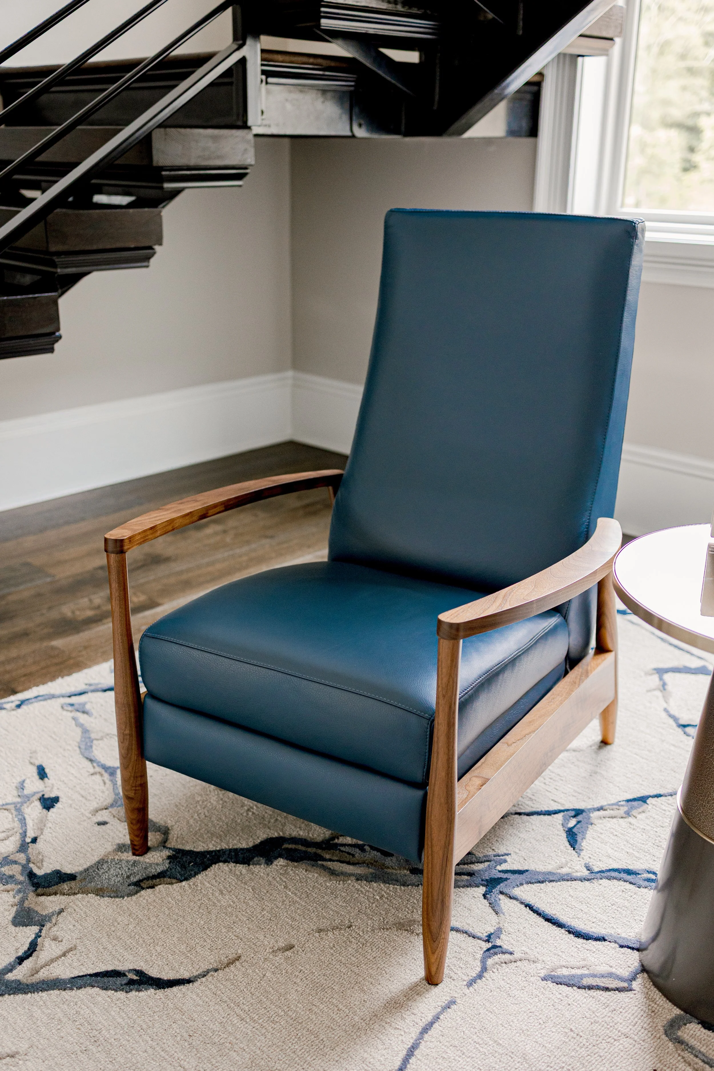 An intimate sitting area designed with comfort and intention underneath a cascading, floating staircase, offering a cozy retreat within the home. Carefully selected seating, layered textiles, and warm tones create a space ideal for quiet moments or r