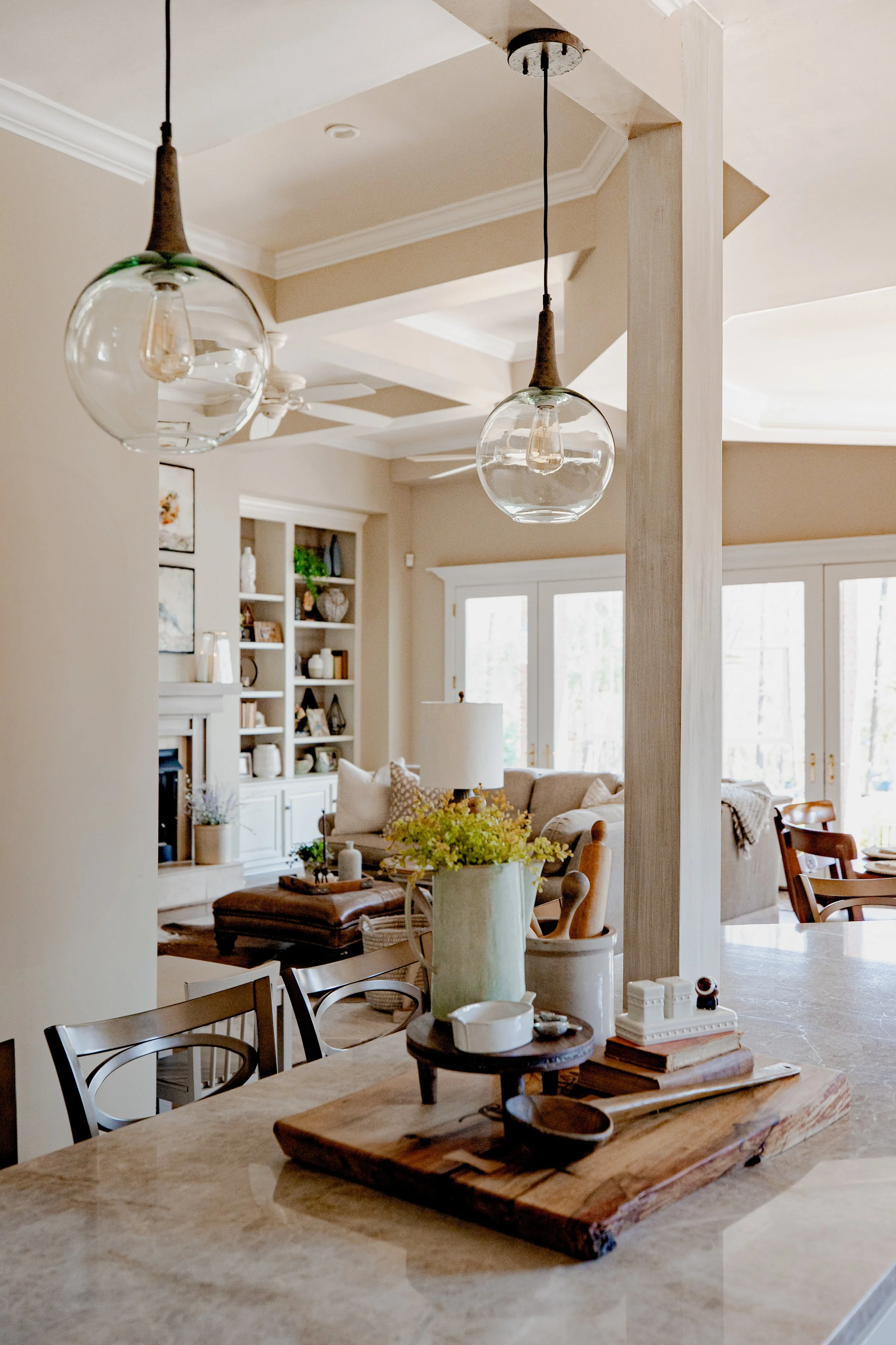 View of the warm and inviting living room/den by Cossart Design from the luxury kitchen, featuring a cozy fireplace, built-in bookcases, and rich textures throughout. The design blends comfort and luxury, with layered furnishings, custom accents, and