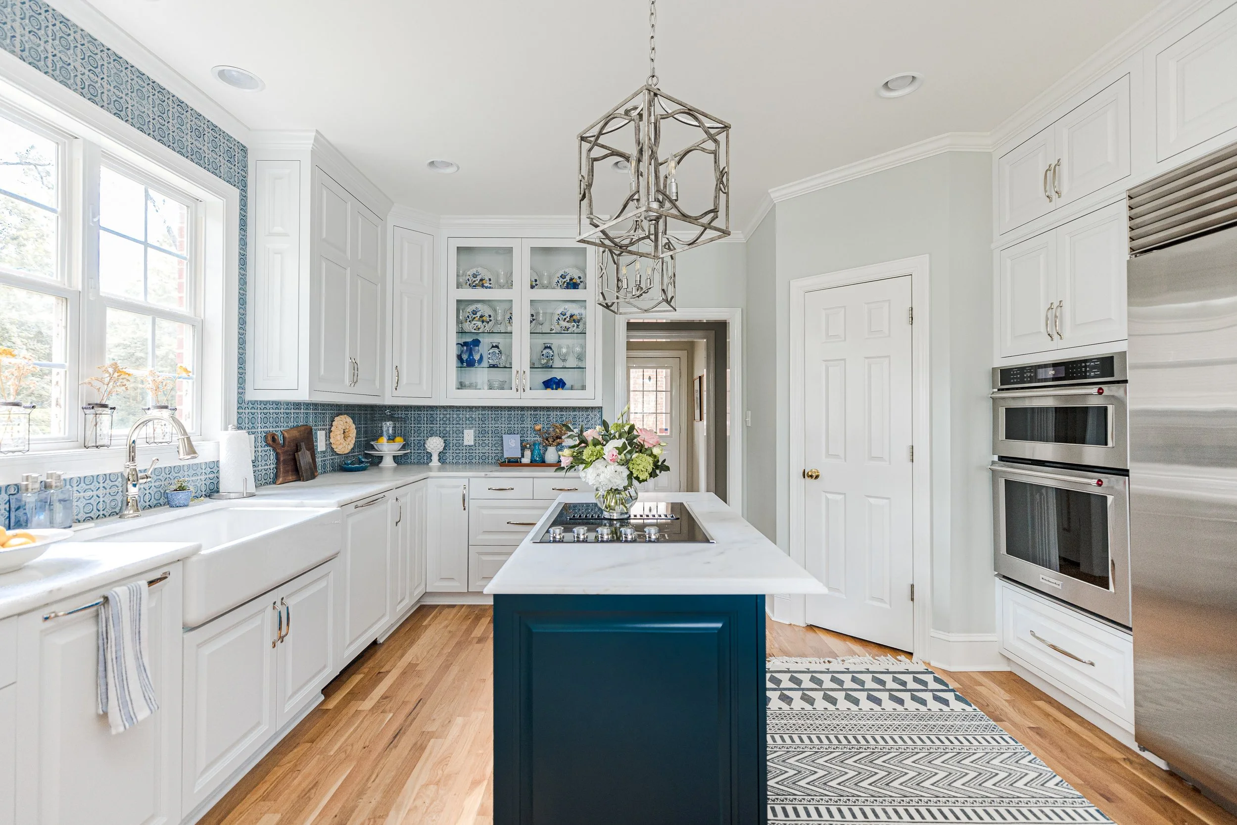 A bright, functional, and stylish kitchen designed by Cossart Design, featuring crisp white cabinetry, custom backsplash, and playful blue accents. Thoughtfully selected finishes and layout make this kitchen ideal for cooking, entertaining, and daily