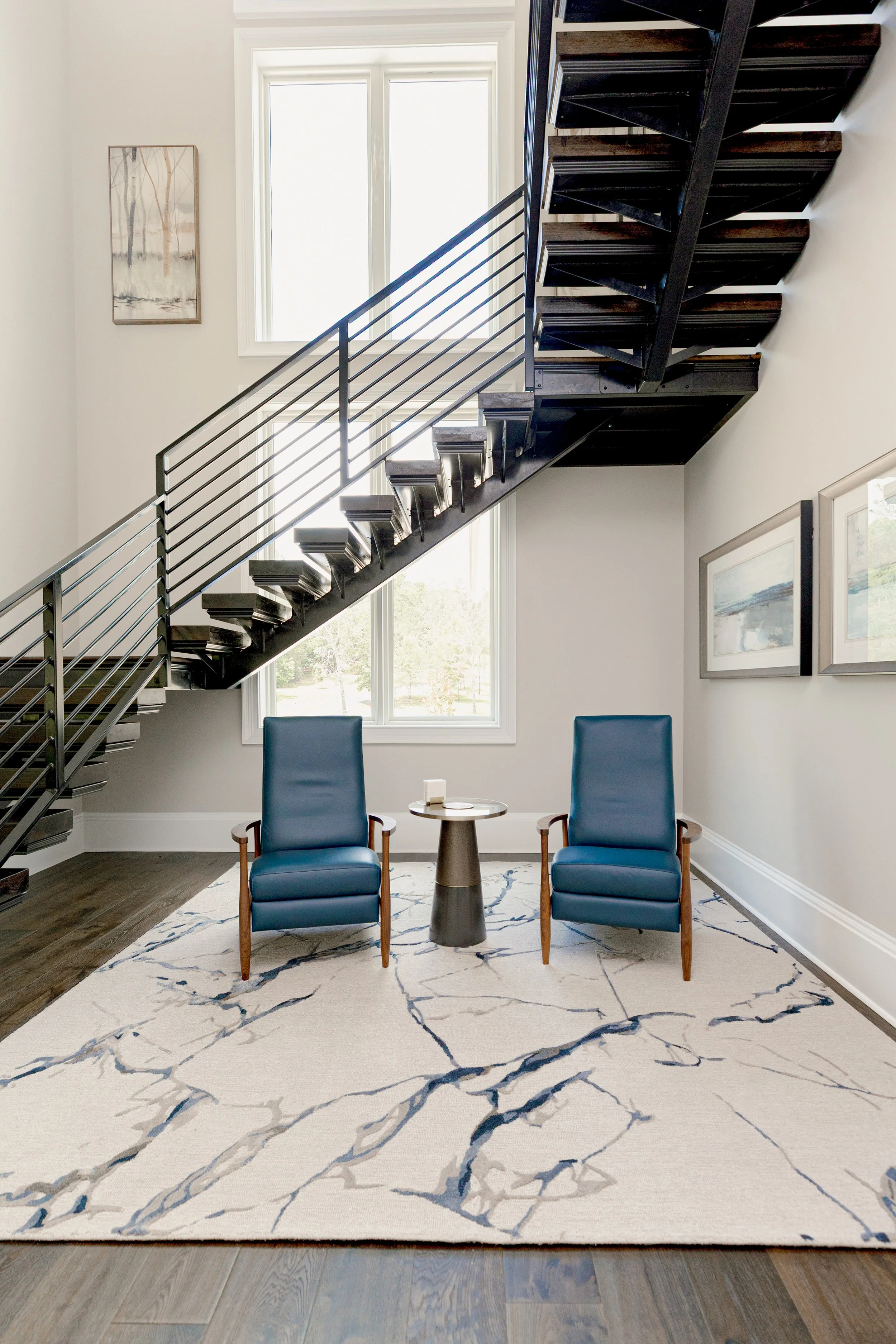 An intimate sitting area designed with comfort and intention underneath a cascading, floating staircase, offering a cozy retreat within the home. Carefully selected seating, layered textiles, and warm tones create a space ideal for quiet moments or r