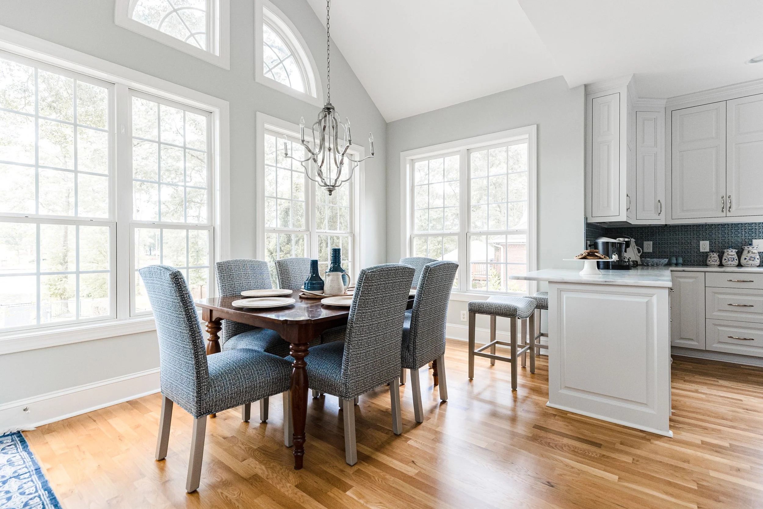 A sunlit eat-in dining area by Cossart Design, featuring expansive windows, elegant furnishings, and thoughtful details that create a bright, inviting space for meals and gatherings. The design balances Southern charm with elevated style, perfect for