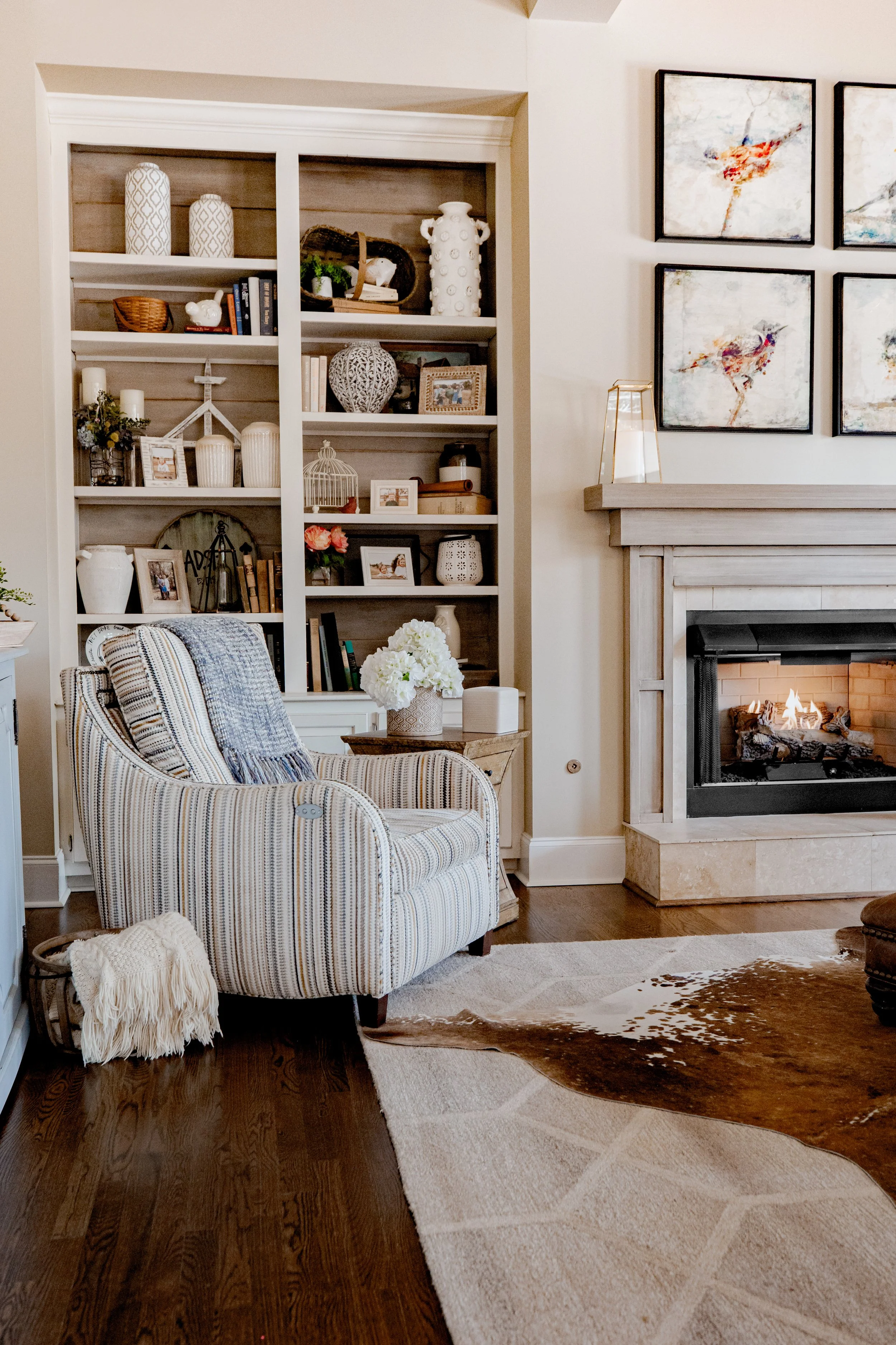 A warm and inviting living room/den by Cossart Design, featuring a cozy fireplace, built-in bookcases, and rich textures throughout. The design blends comfort and luxury, with layered furnishings, custom accents, and thoughtful layout that make the s