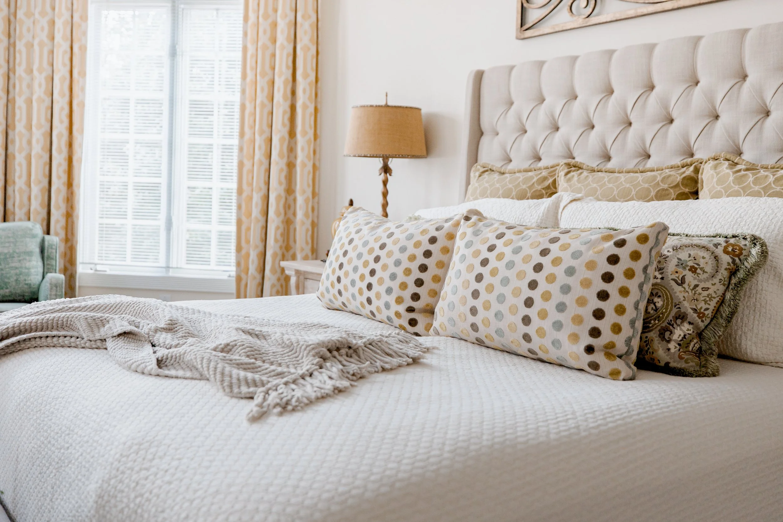 A serene and luxurious master bedroom designed by Cossart Design, featuring layered textures, custom bedding, and thoughtfully curated furnishings. The space balances elegance and comfort with warm tones, soft lighting, and functional seating areas t