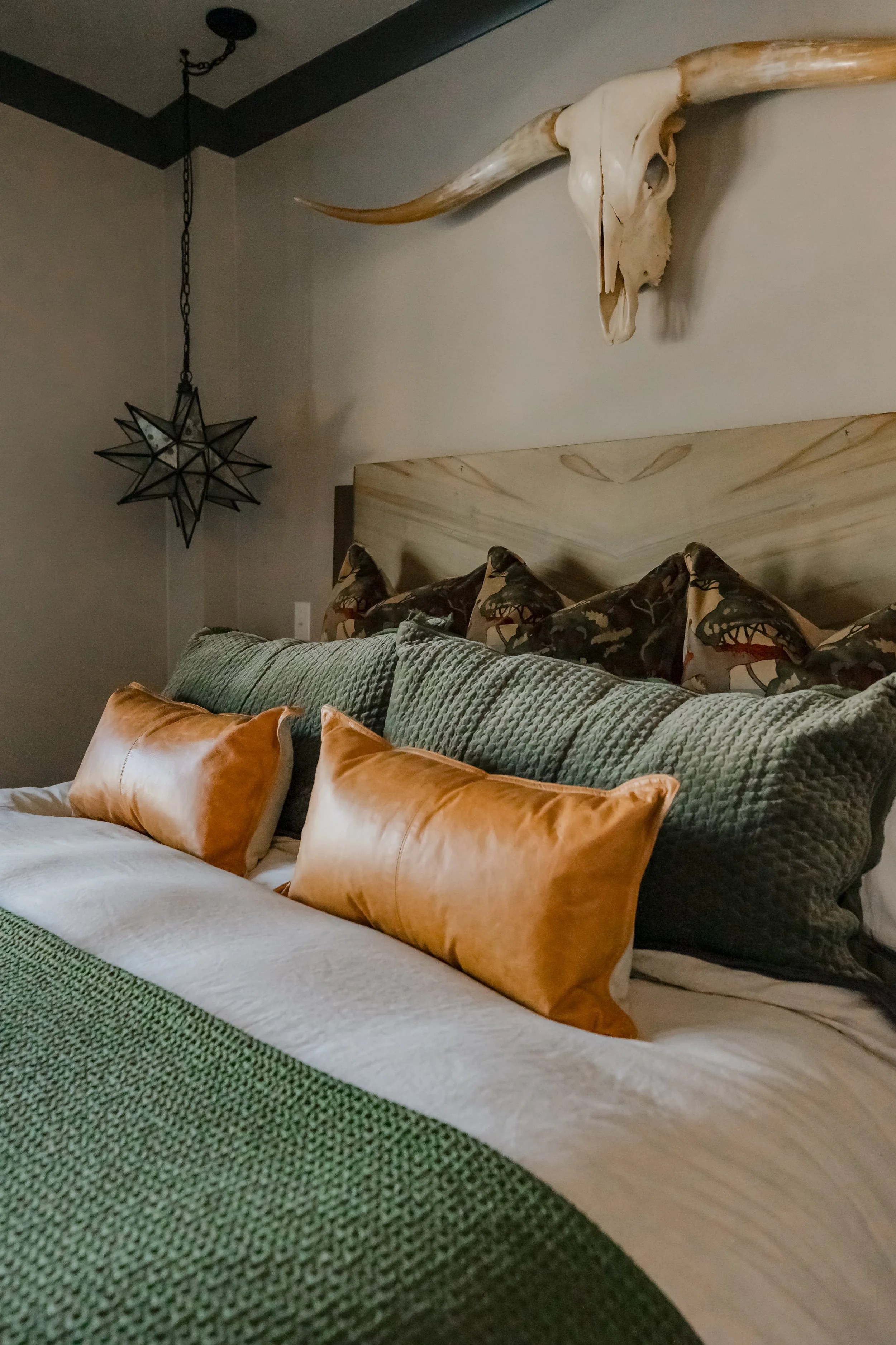 A luxurious master bedroom retreat designed by Cossart Design, featuring custom pillows and carefully layered textiles that add warmth and personality to this masculine lodge‑style home. Soft green hues and refined finishes create a calming yet sophi