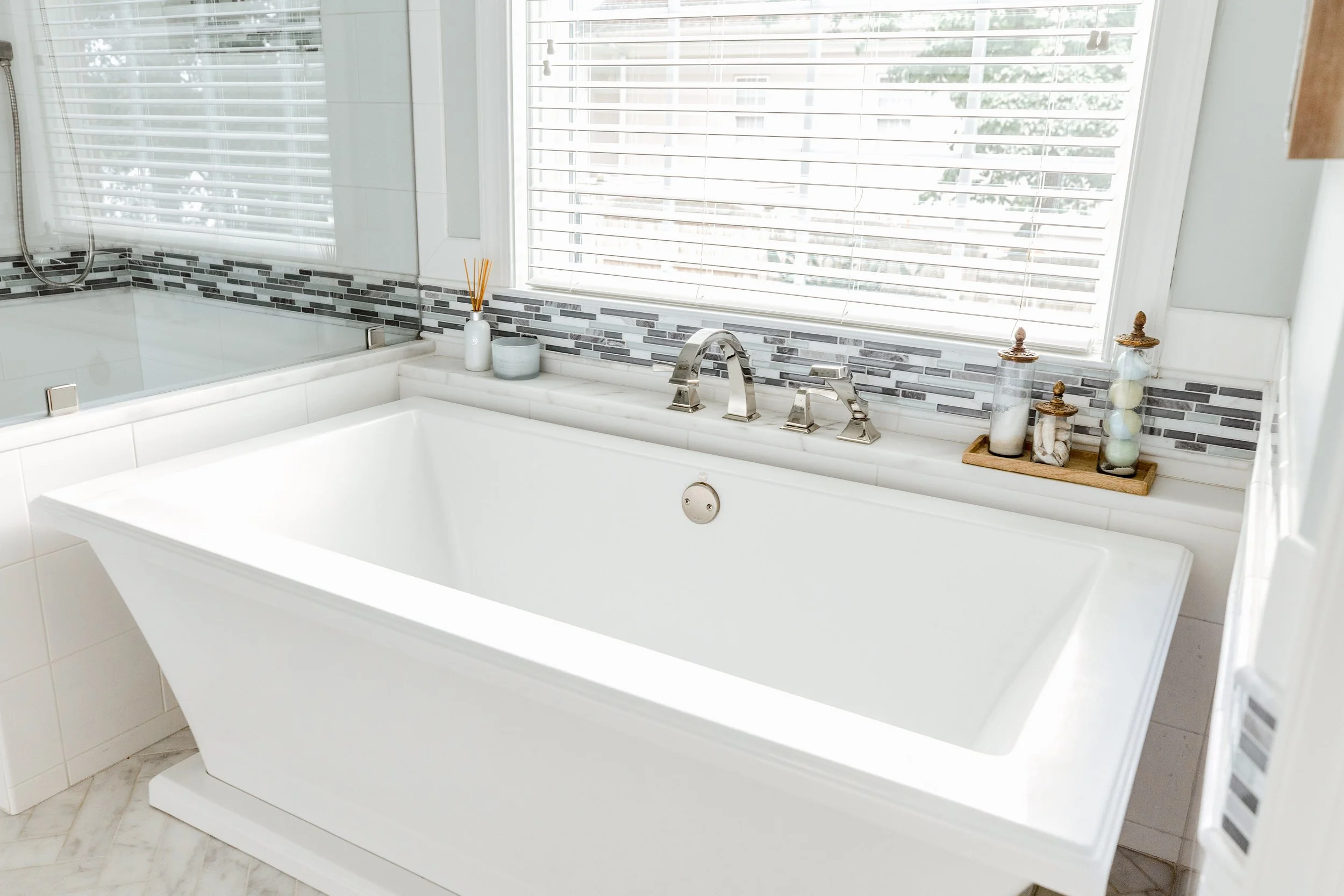 A spa-inspired master bathroom by Cossart Design, featuring custom herringbone floors, white and blue accents, a soaking tub, shower with custom tile, and luxurious gold fixtures. Designed for serenity, function, and elevated style, this space is a p