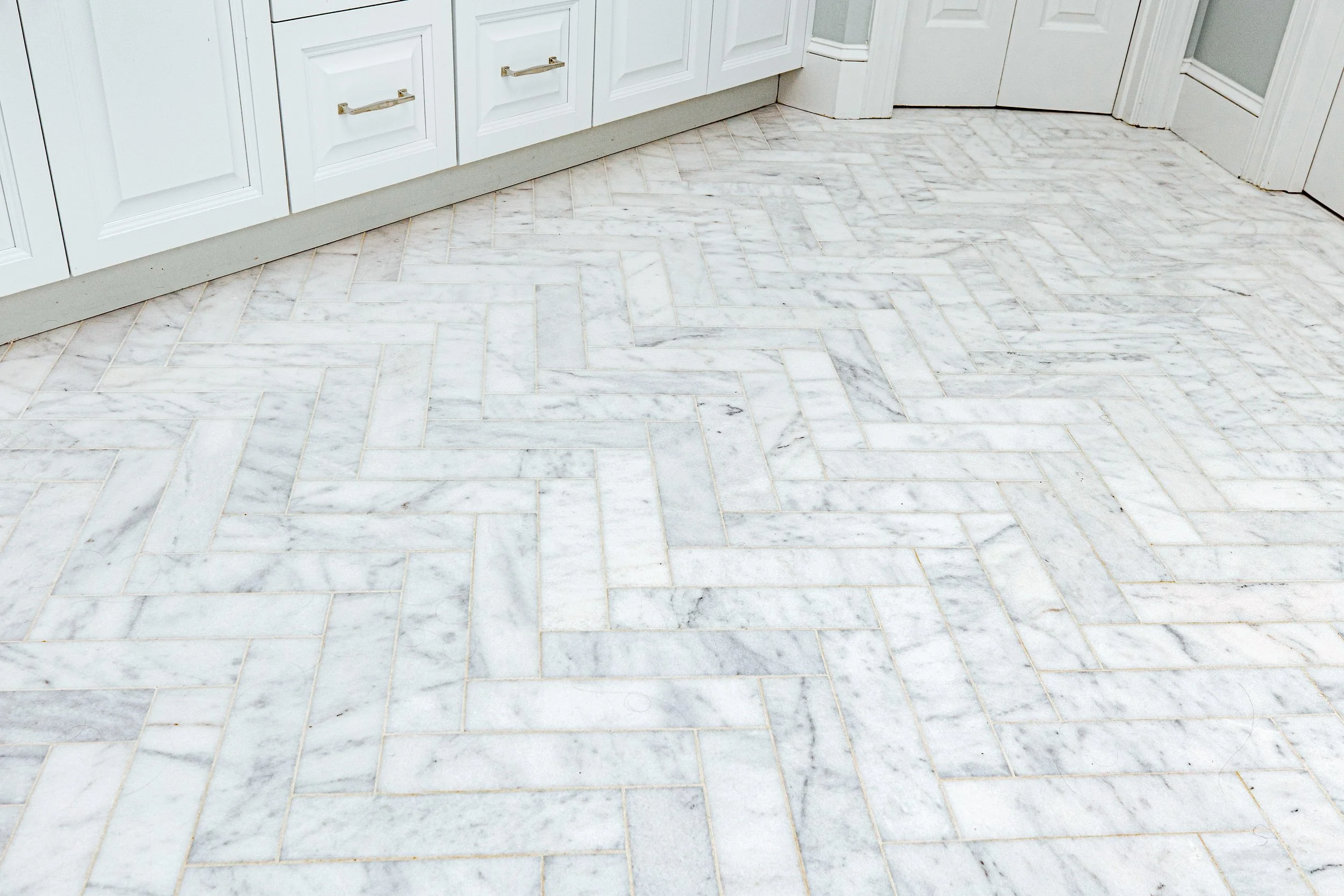 A spa-inspired master bathroom by Cossart Design, featuring custom herringbone floors, white and blue accents, a soaking tub, shower with custom tile, and luxurious gold fixtures. Designed for serenity, function, and elevated style, this space is a p