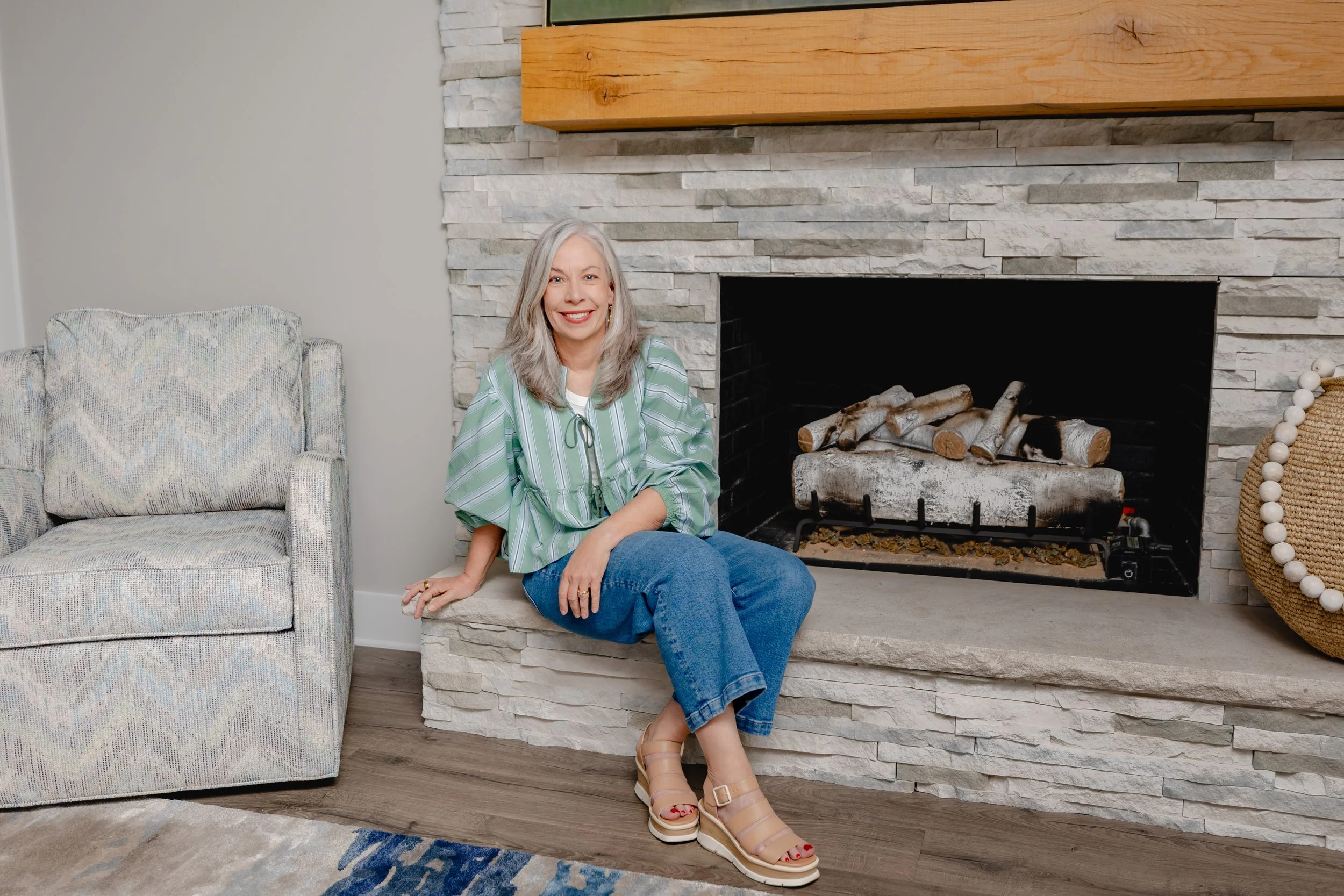 Trish Cossart of Cossart Design seated on a fireplace hearth in a luxury residential home in Perry, GA, featuring custom furniture, layered textures, and Southern-inspired design.