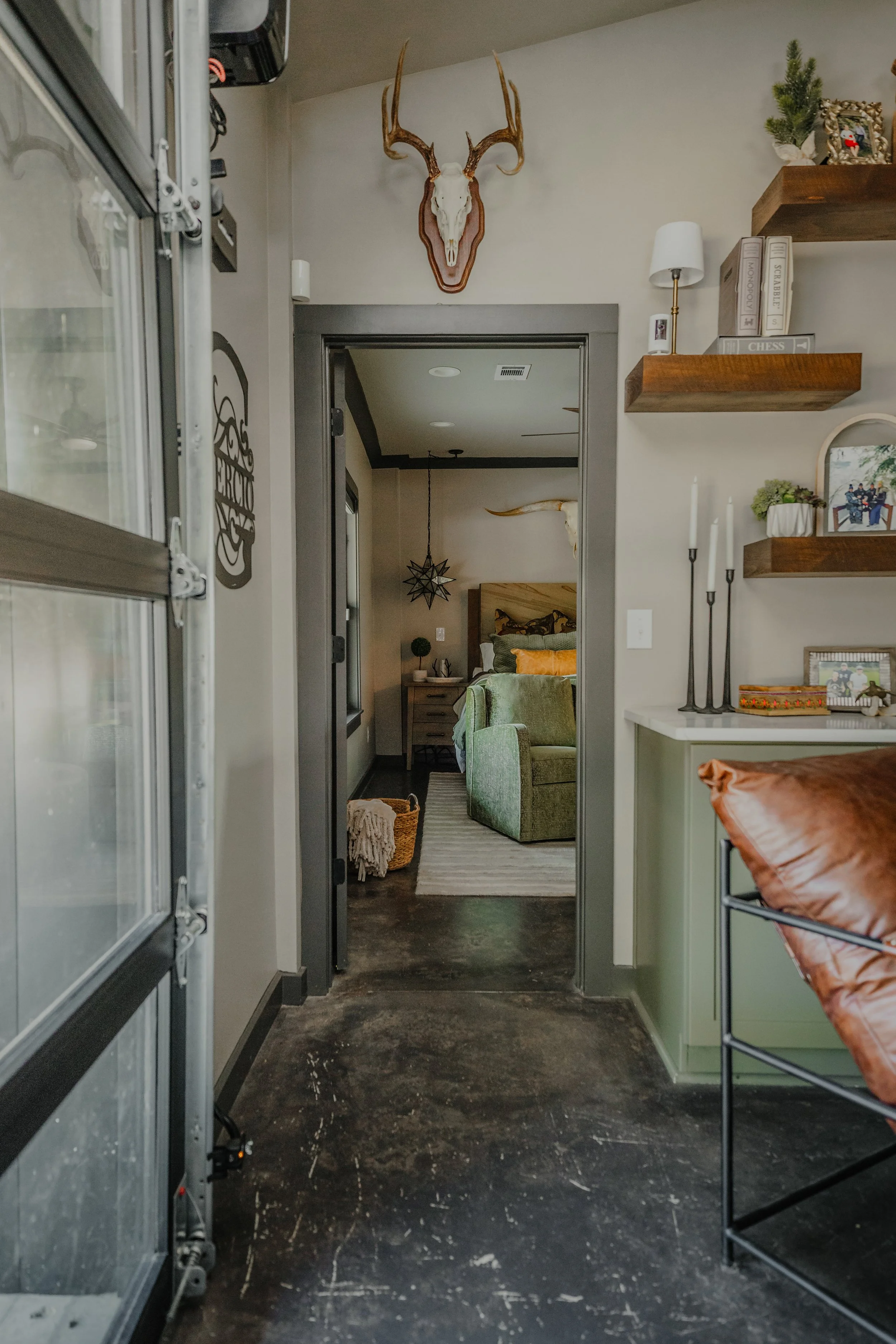 A striking open concept living space by Cossart Design in this Hawkinsville, GA barndominium that masterfully blends industrial accents with masculine design. Rich green and wood tones, along with modern tailored furnishings create a lodge‑inspired e