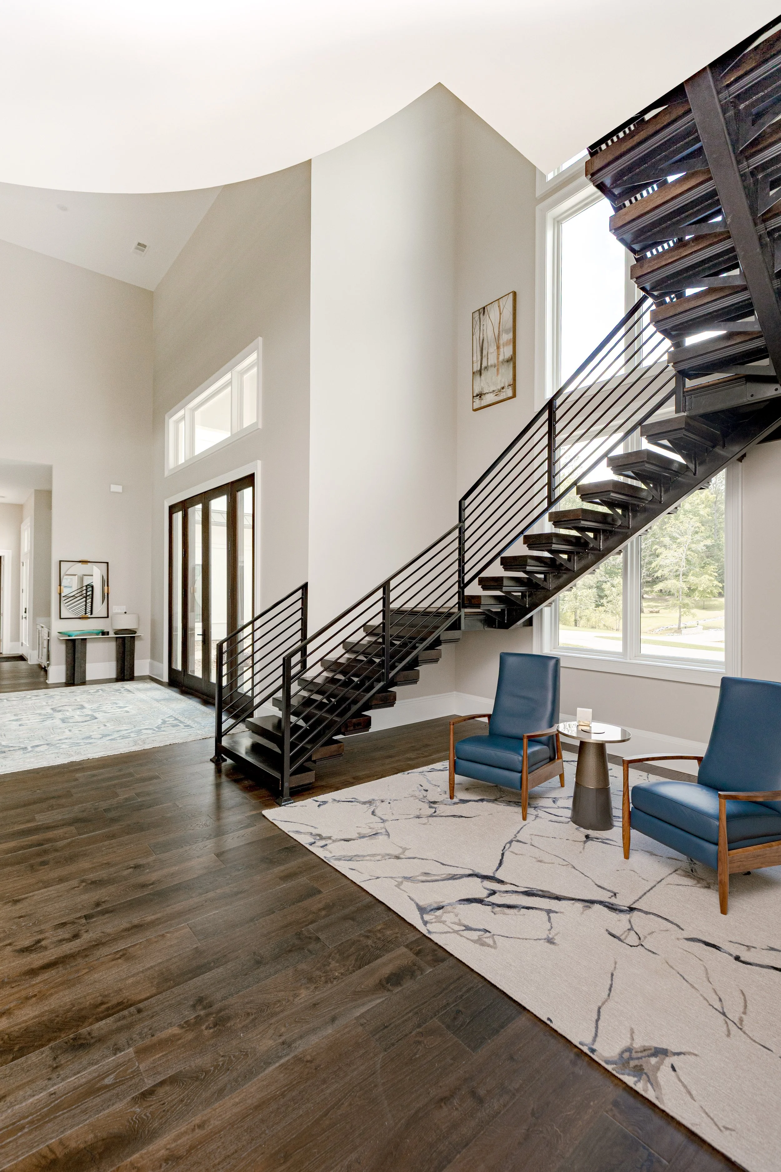 An intimate sitting area designed with comfort and intention underneath a cascading, floating staircase, offering a cozy retreat within the home. Carefully selected seating, layered textiles, and warm tones create a space ideal for quiet moments or r