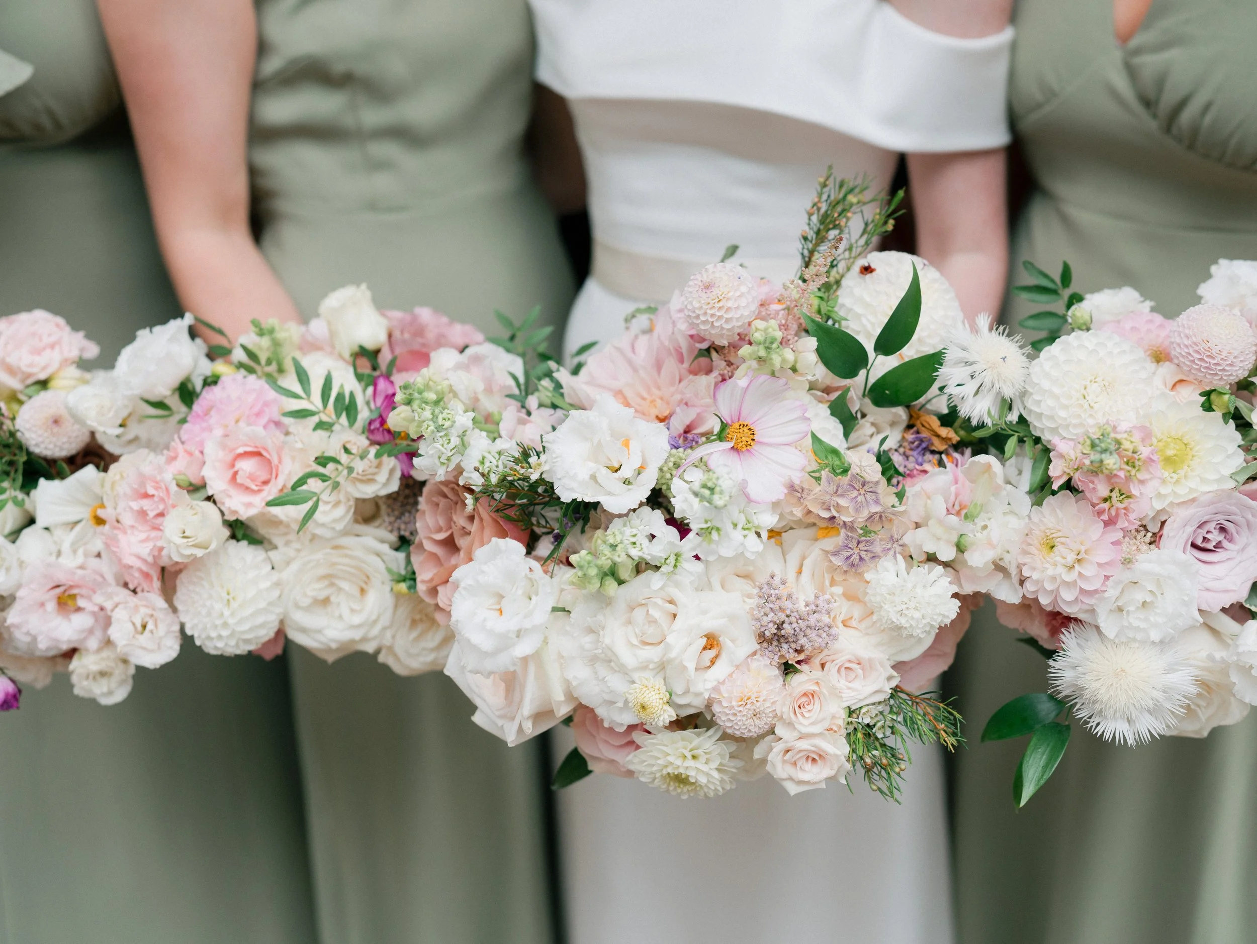 A bride and bridesmaids holding large bouquets of pink and white flowers at a wedding.