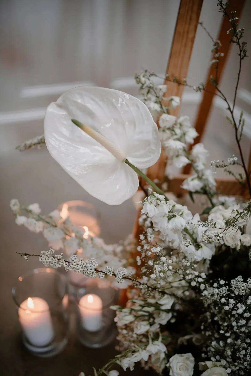 close up of white anthurium flower and other delicate white flowers. a cluster of lit candles visible in the background.  