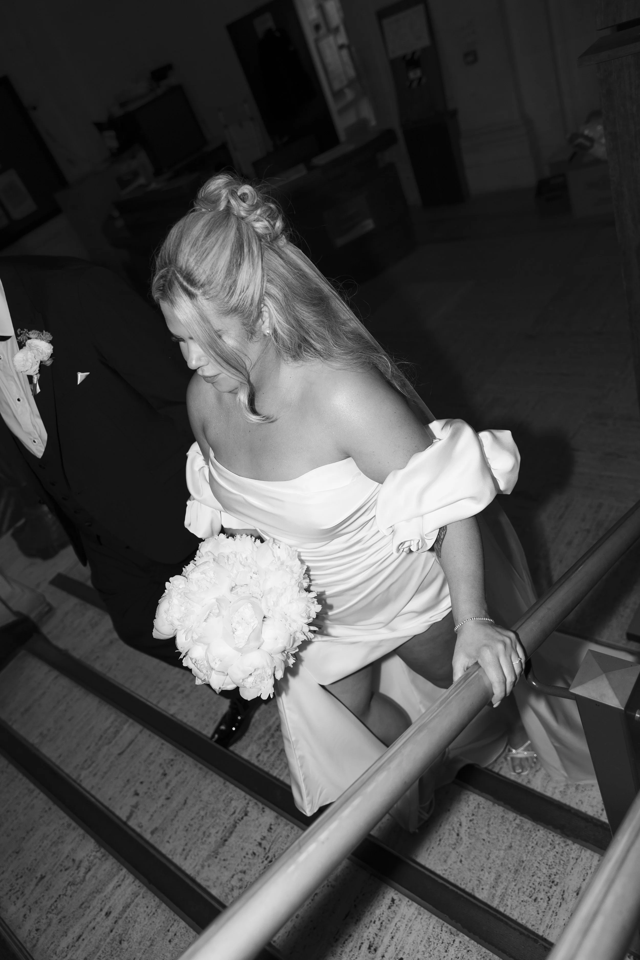 A bride in a strapless wedding dress holding a bouquet of flowers moving down a staircase.